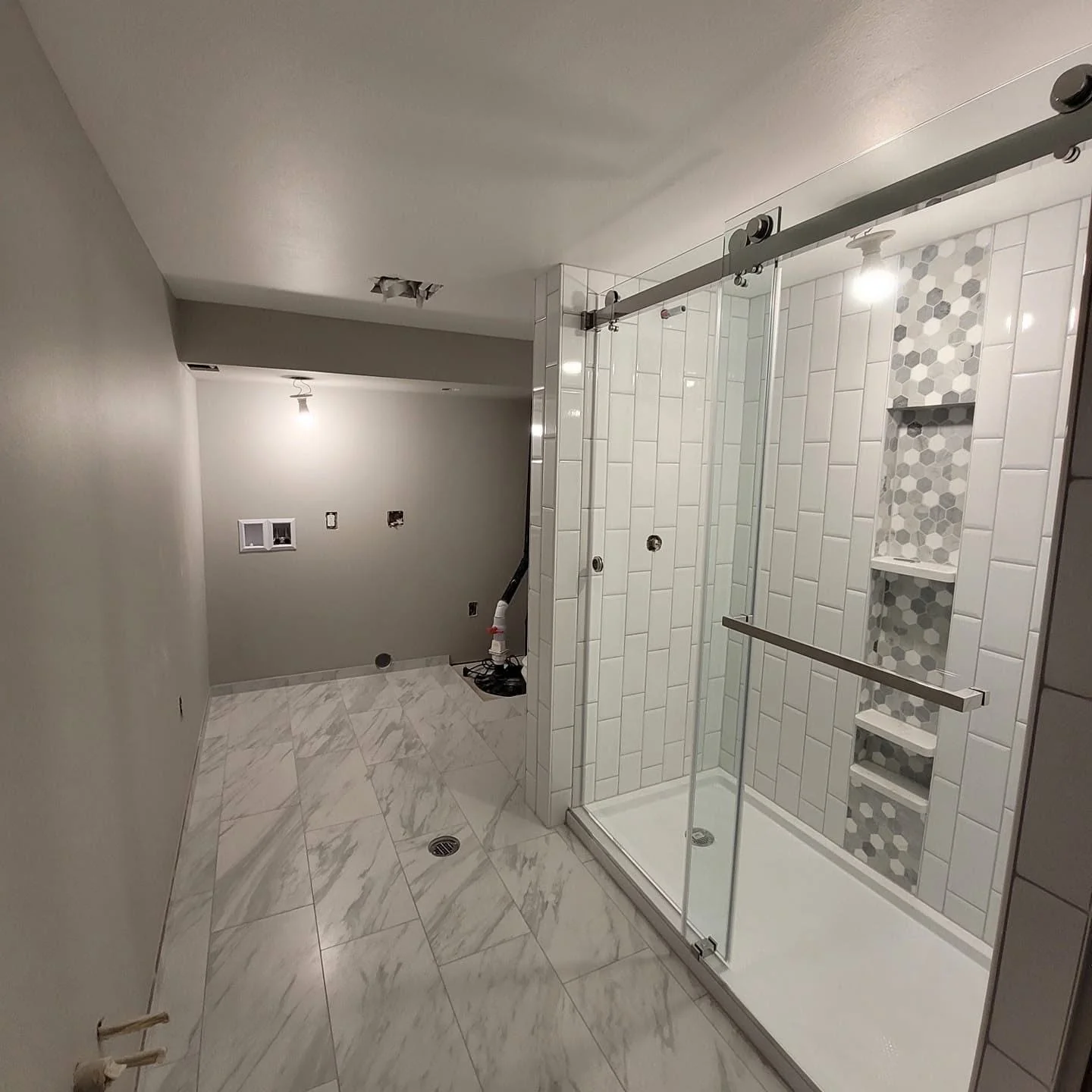 Bathroom under construction with a glass shower enclosure, white subway tiles, and marble flooring.