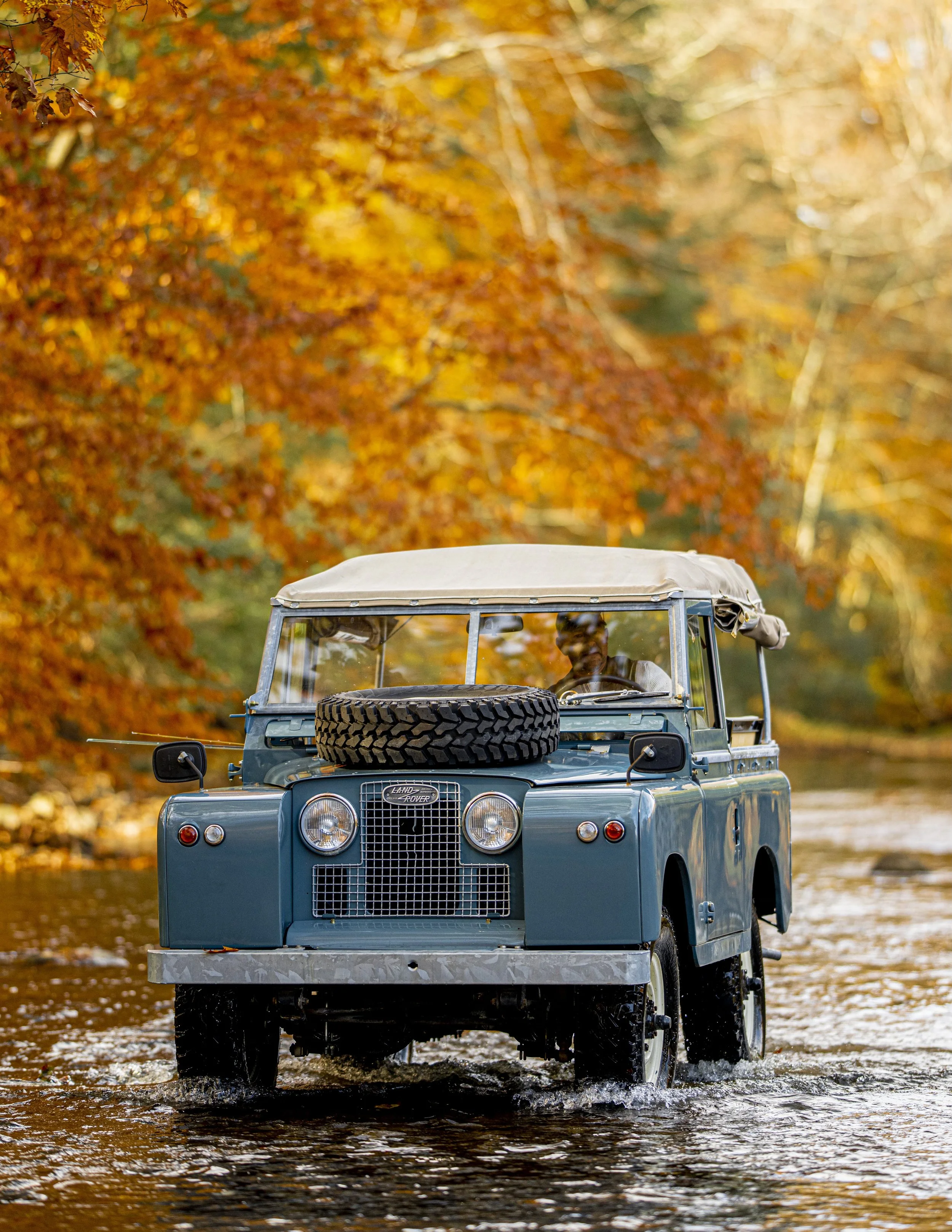 Vintage marine blue Land Rover Series II 1959 truck driving through creek in Autumn