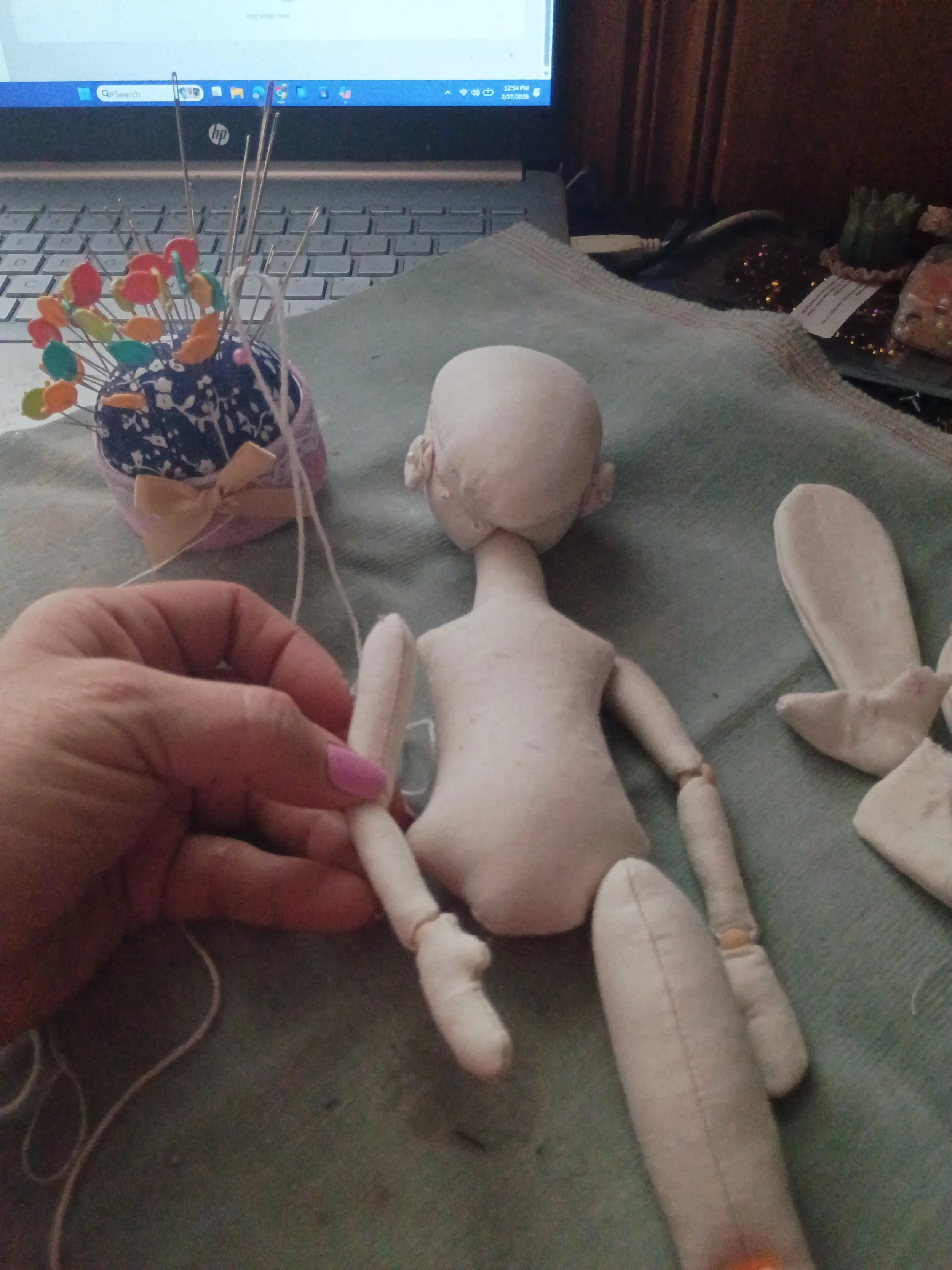 A plush doll lying on a surface, with a computer keyboard and screen in the background, and a container with colorful pushpins nearby.