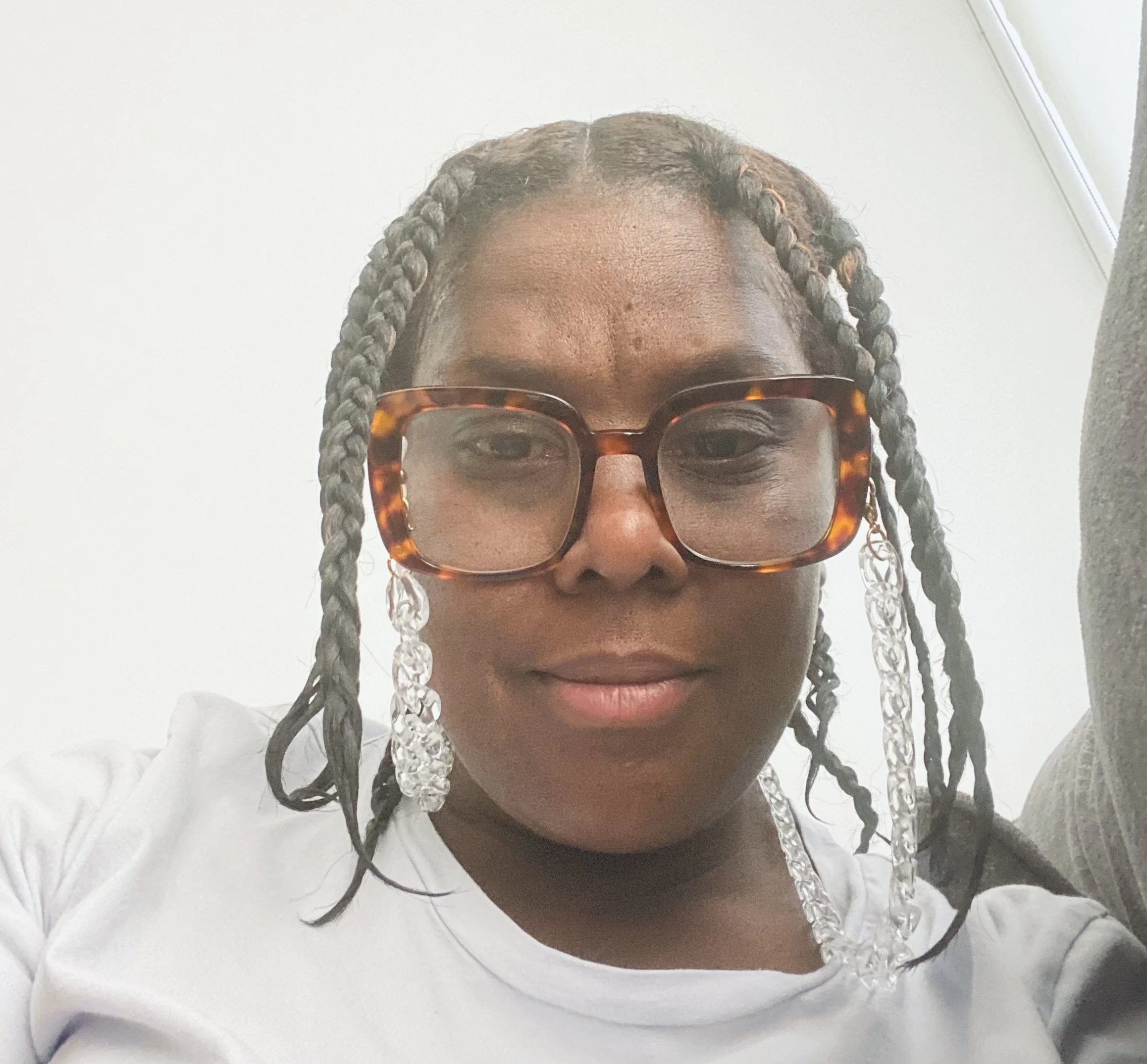 Close-up of a woman with braided hair wearing tortoiseshell glasses, partially visible face, white background.