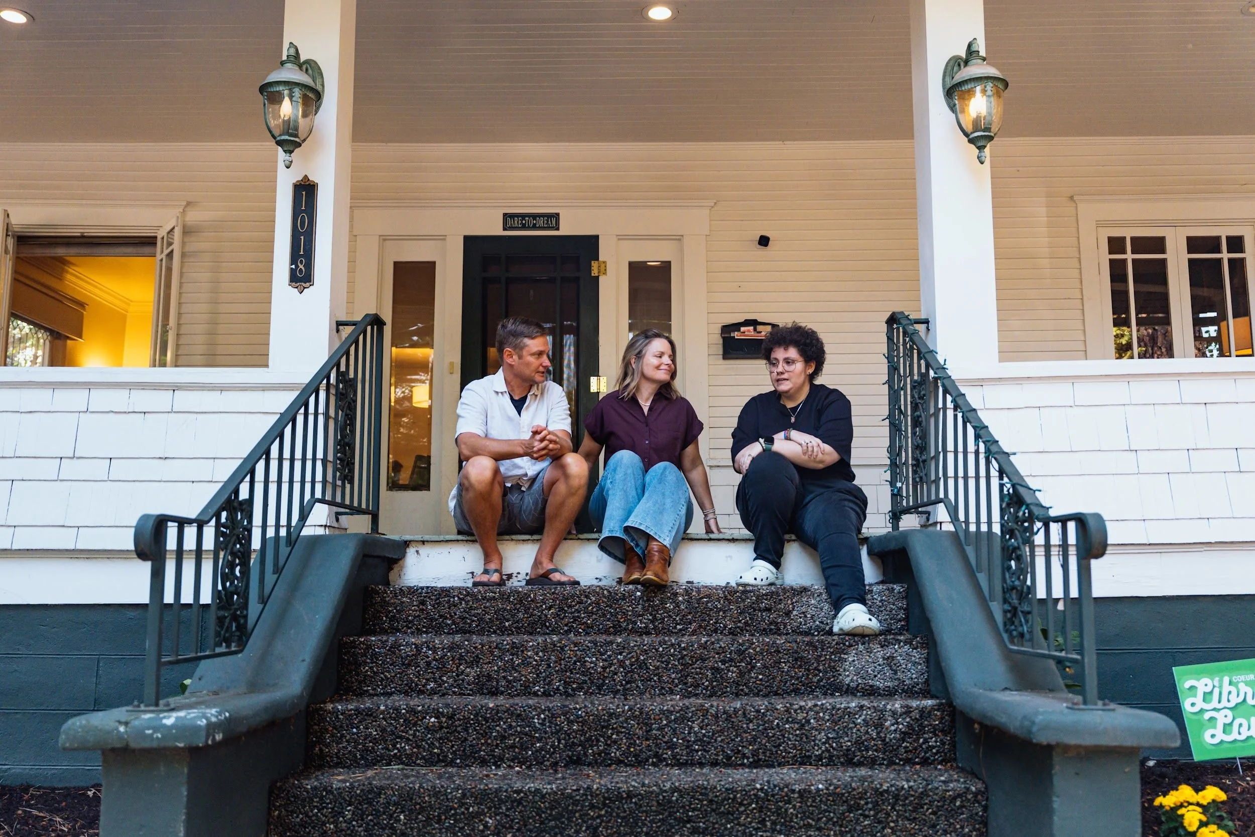 Three adults sitting together and talking on the front steps of a white house