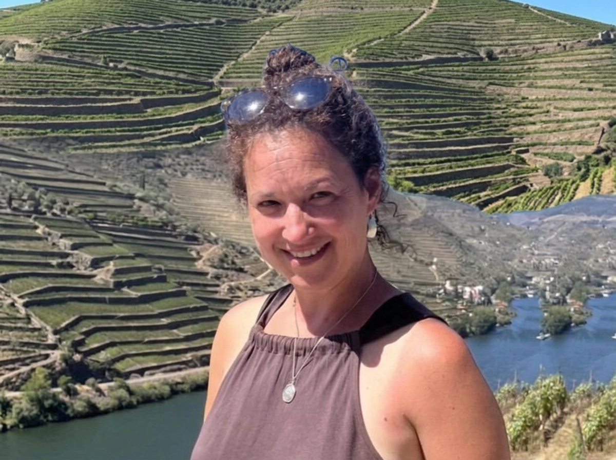 A woman smiling at the camera with vineyard terraces and a river in the background.