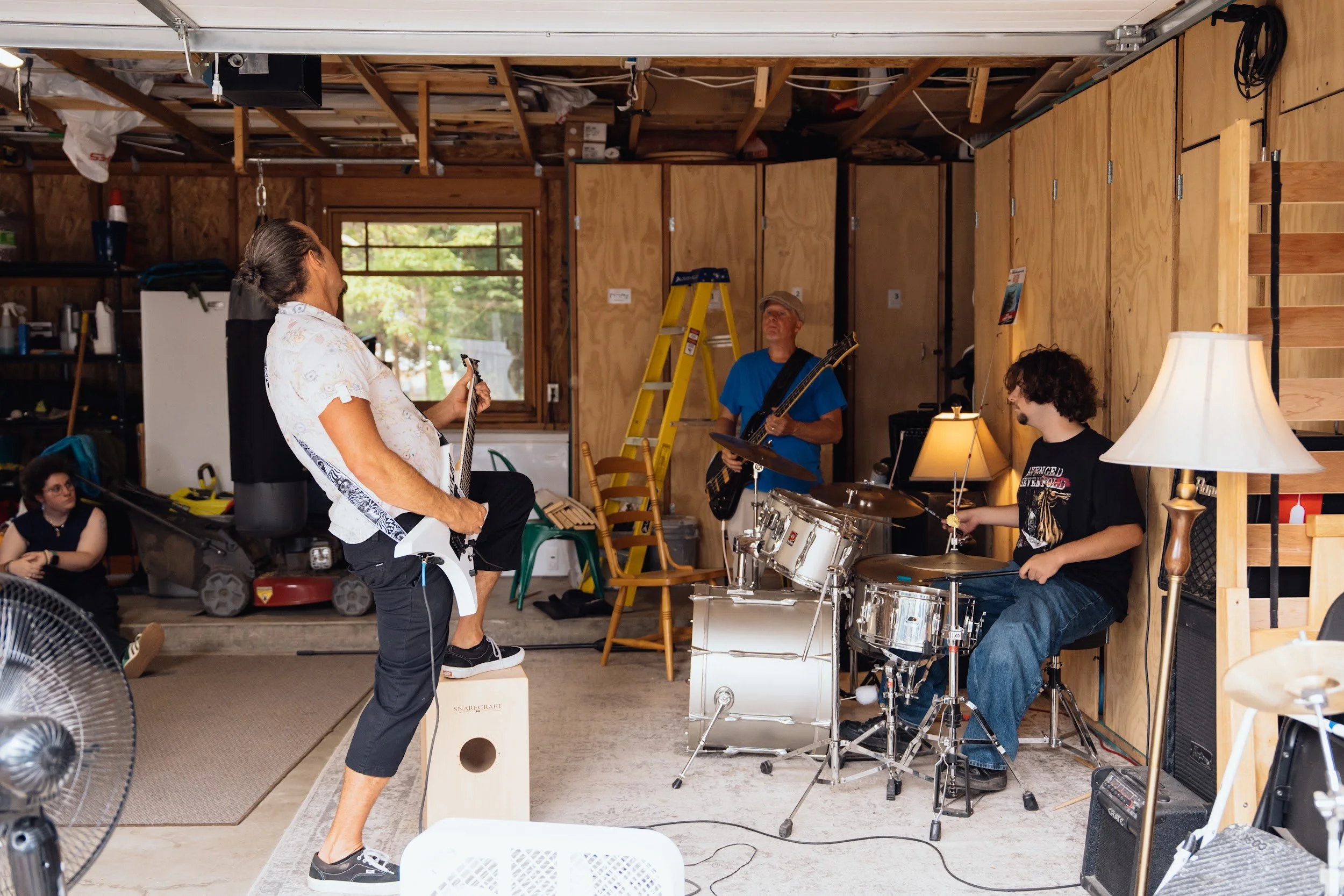 Band practice in a garage with guitars, a drum kit, and a cajon