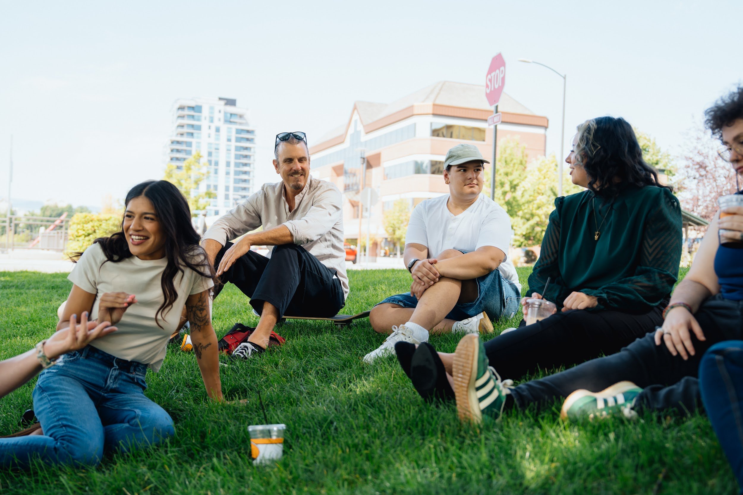 Smiling adults sitting together on the grass in a city park with coffee