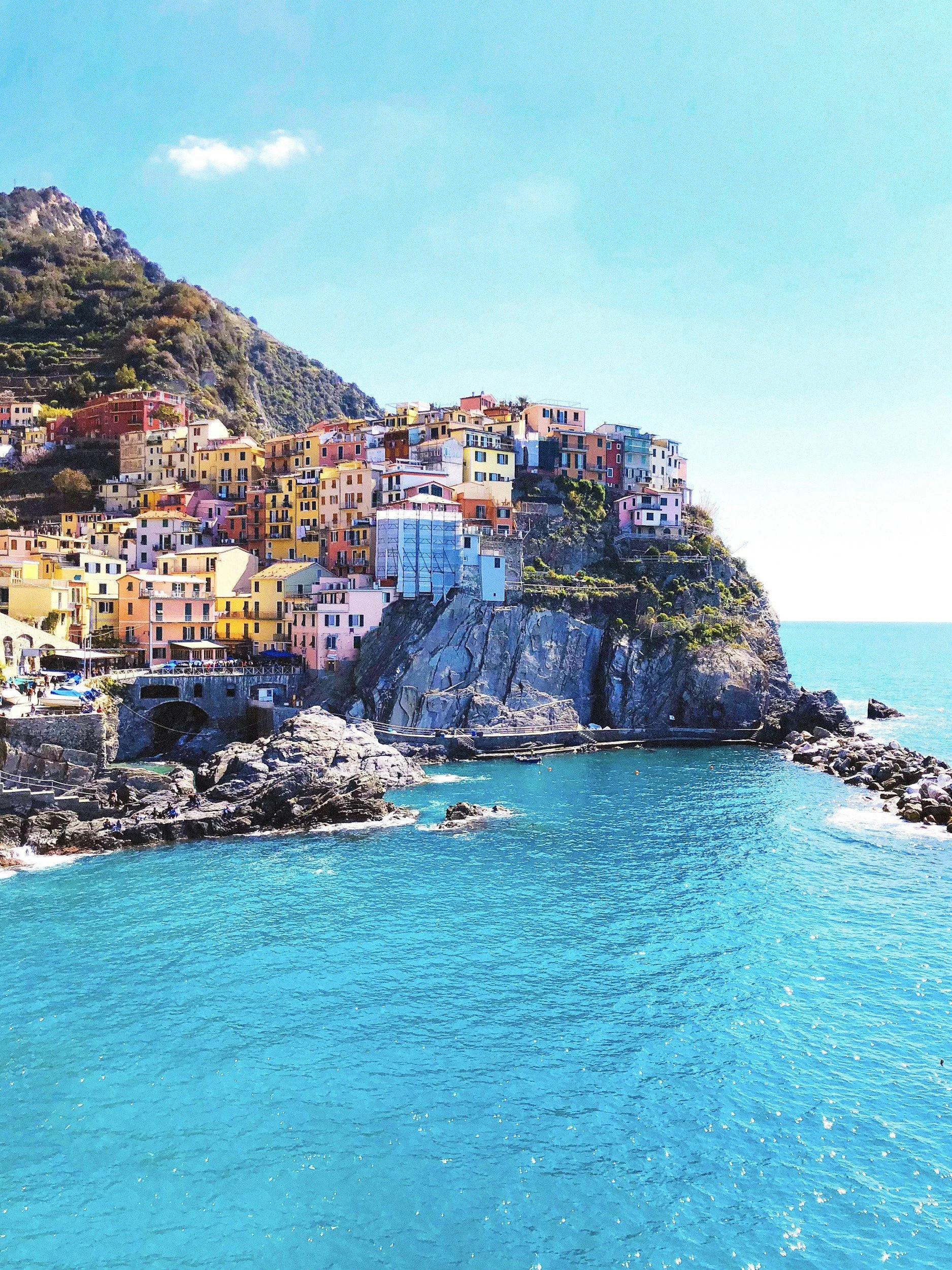 Colorful buildings on a rocky cliff overlooking a bright blue ocean under a clear sky.