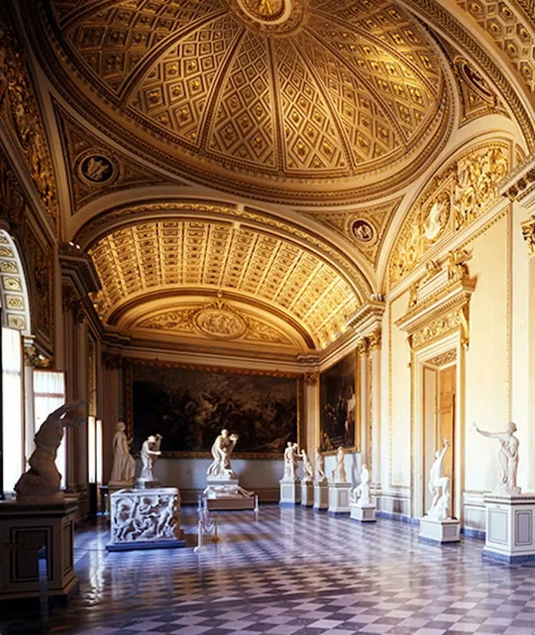 Interior of a grand art gallery with ornate gold ceiling, framed paintings, and classical sculptures displayed on pedestals.