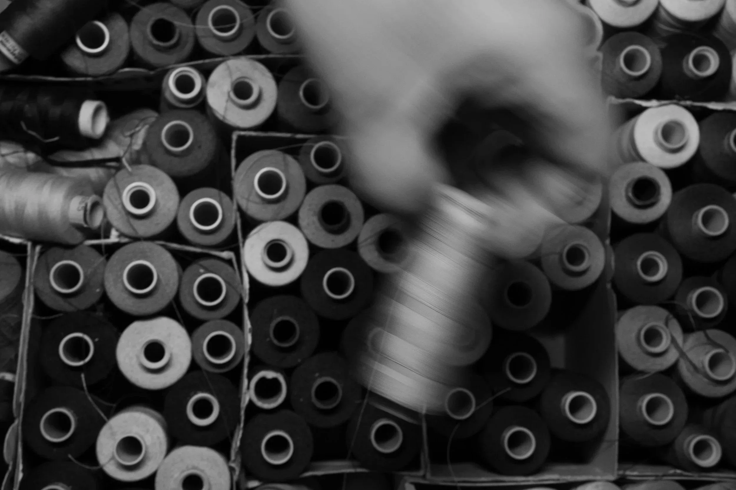 A collection of sewing or knitting yarn spools in a storage bin, viewed from above in black and white.