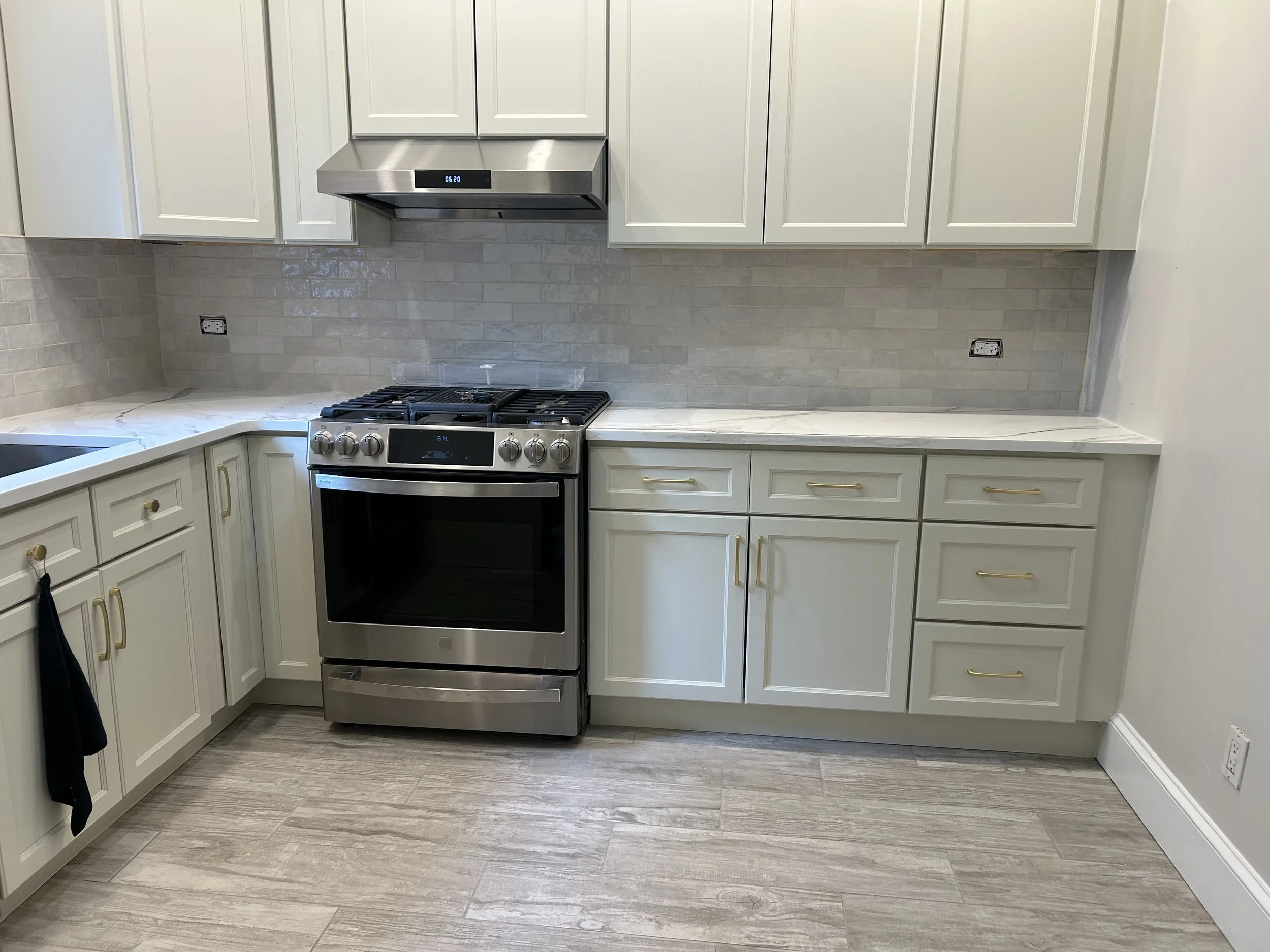 A modern kitchen with white cabinets, a stainless steel stove and range hood, subway tile backsplash, and light gray hardwood floor.