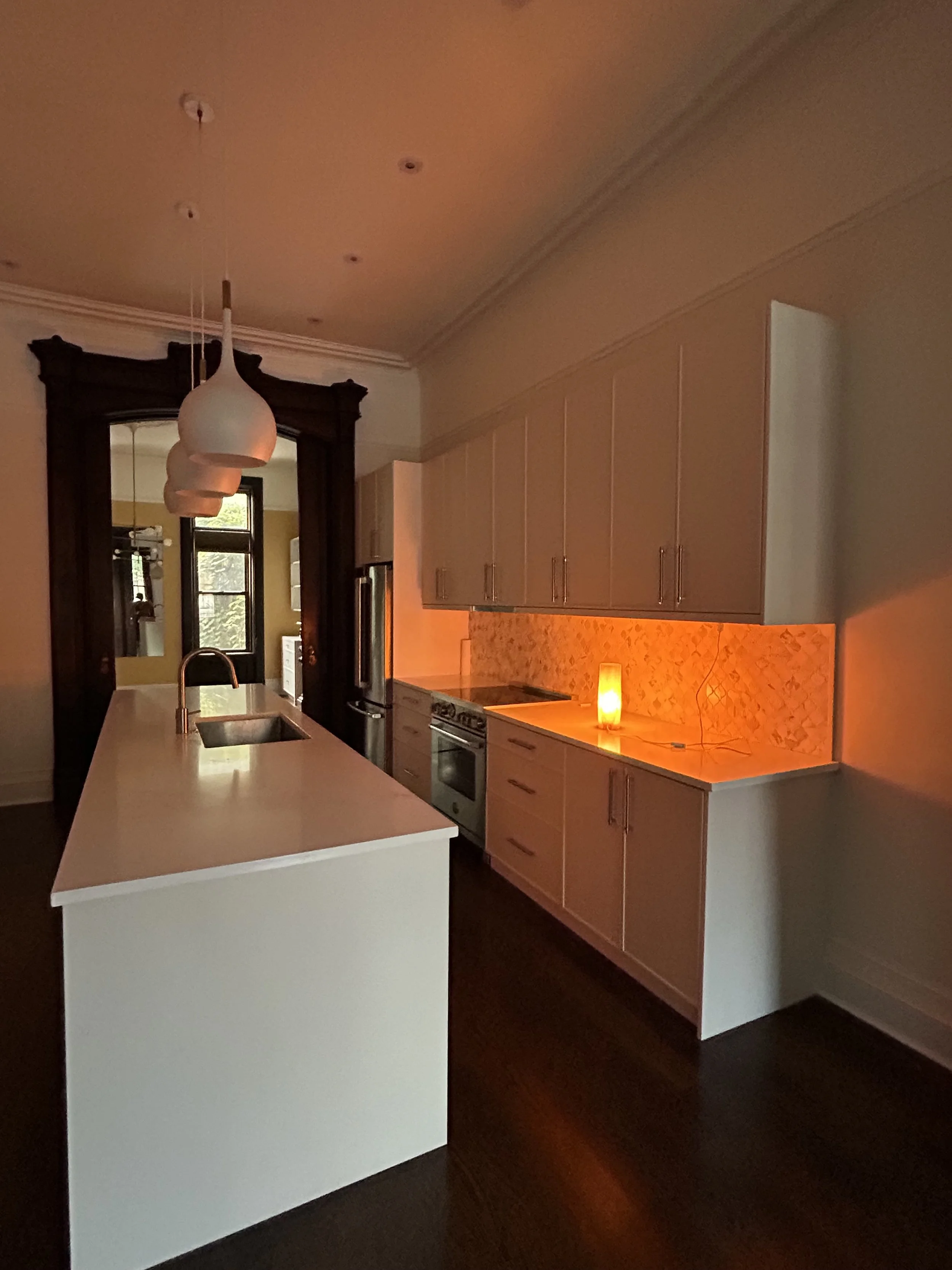 Modern kitchen with white island, black-framed window, white cabinetry, orange backsplash, and a small candle on the counter.