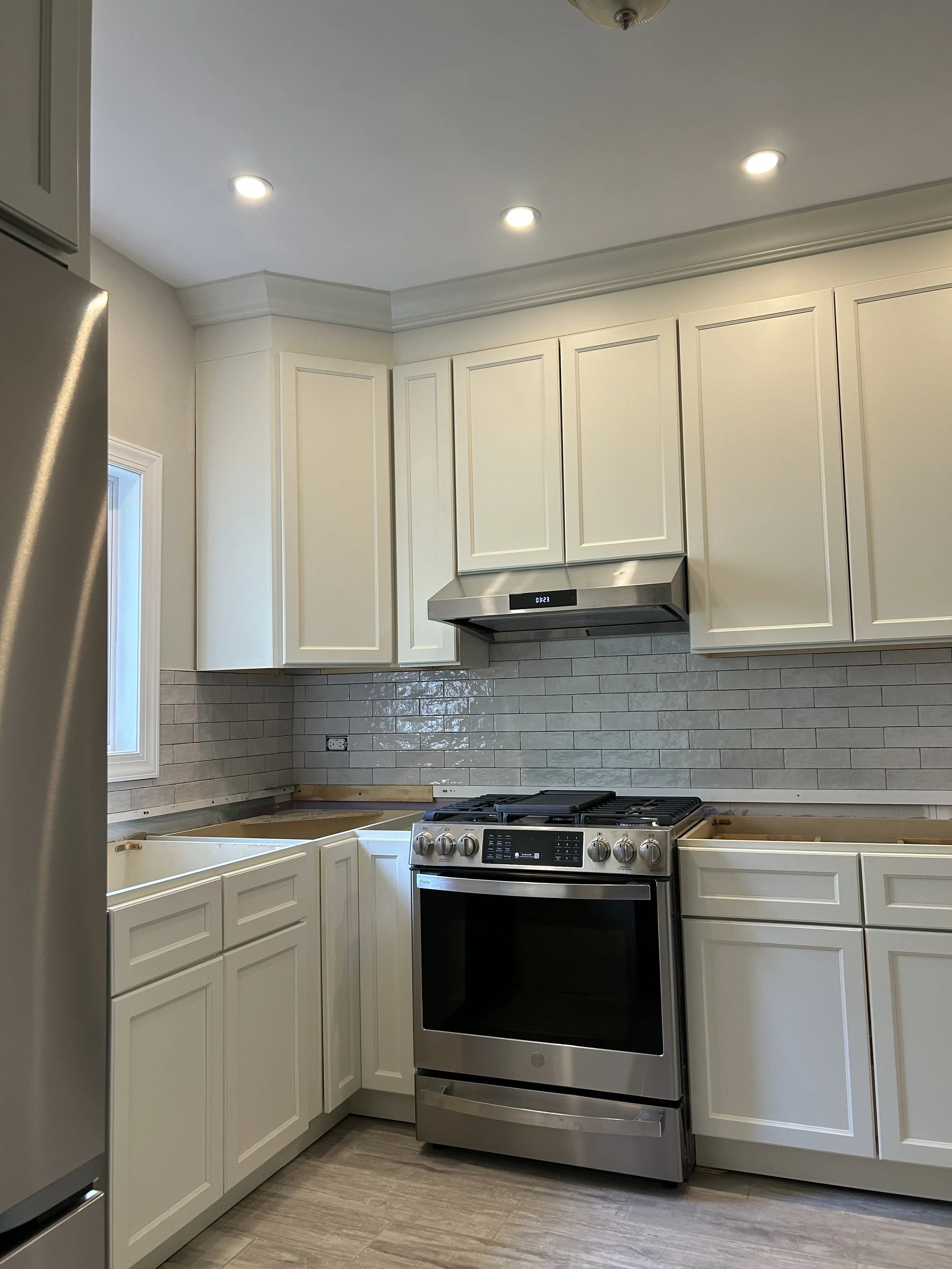 Kitchen with white cabinets, stainless steel stove, gray tile backsplash, and recessed ceiling lights.