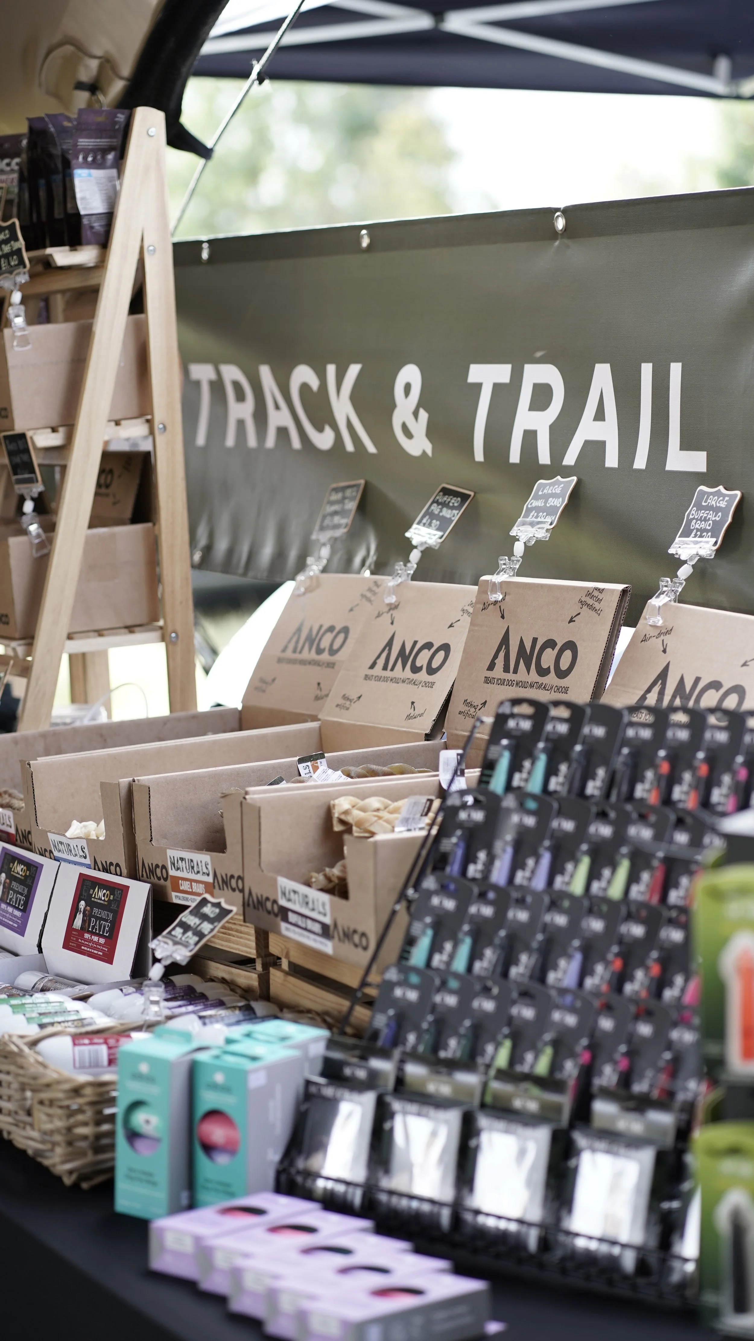 Display of pet supplies at a store, including branded dog treats, grooming products, and accessories under a sign that reads "Track & Trail."