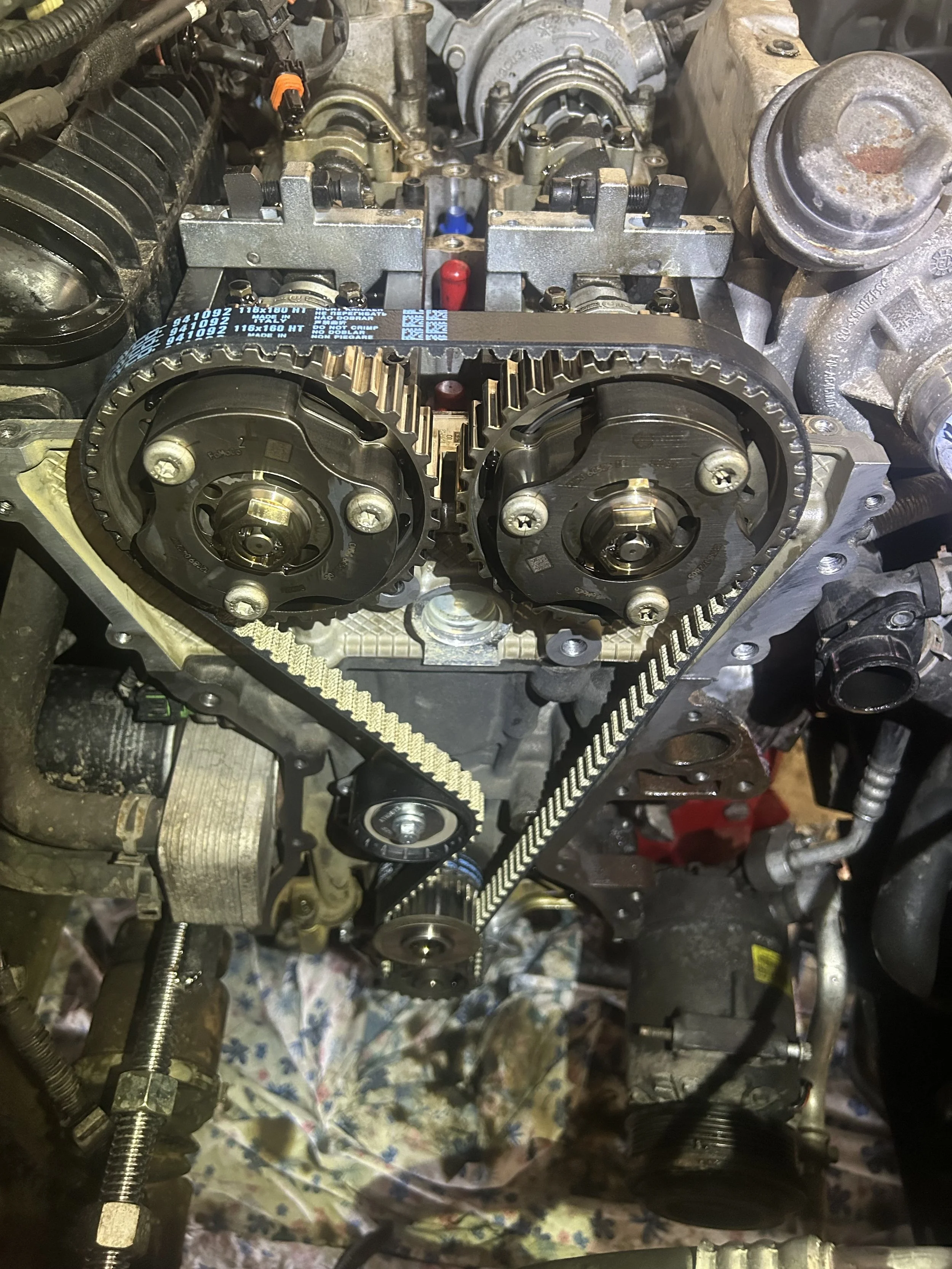 Close-up of a car engine with timing belt, pulleys, and other internal components exposed during repair or maintenance.