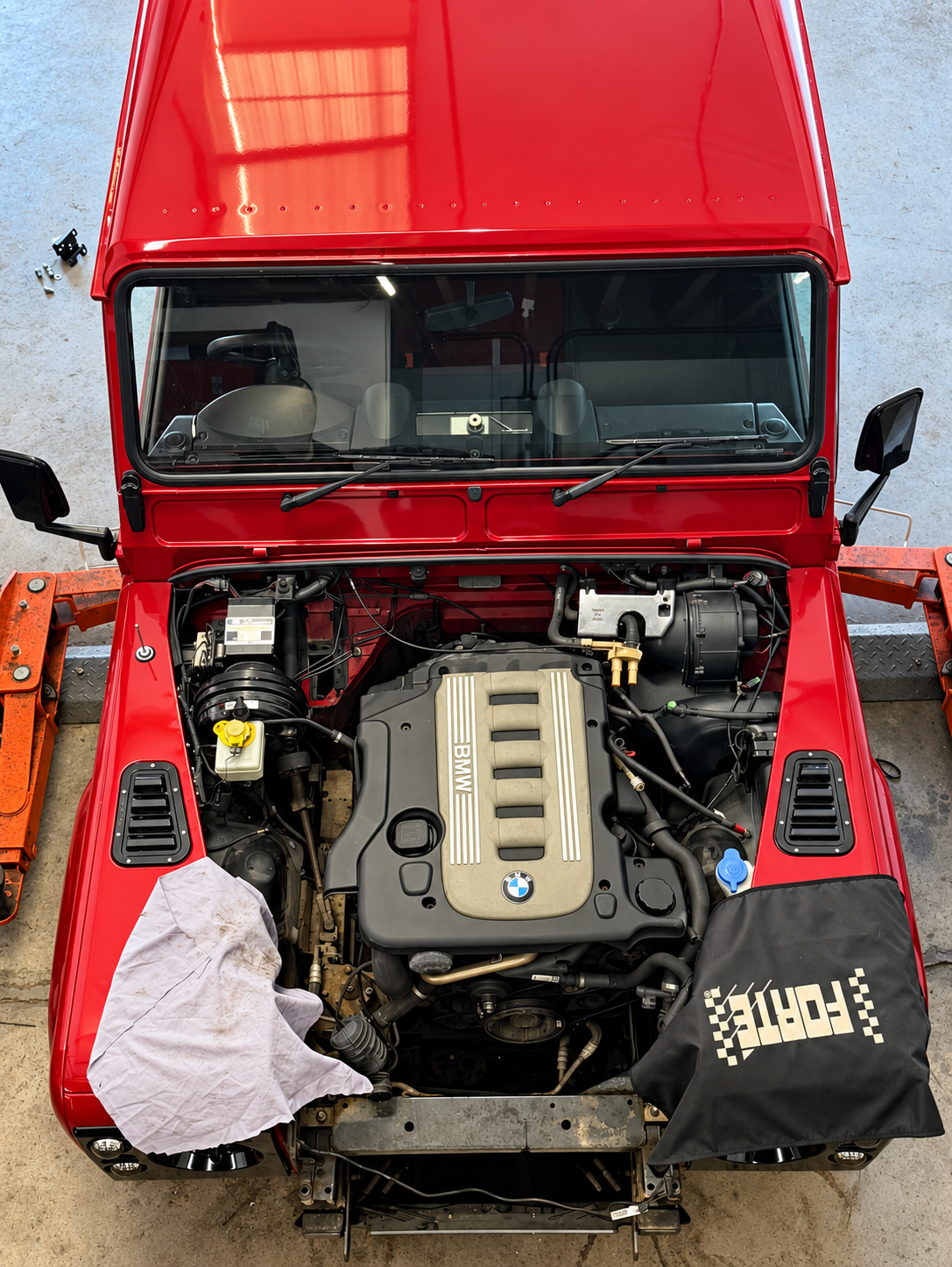 Top view of a red BMW car with the hood open, revealing the engine and engine bay components.