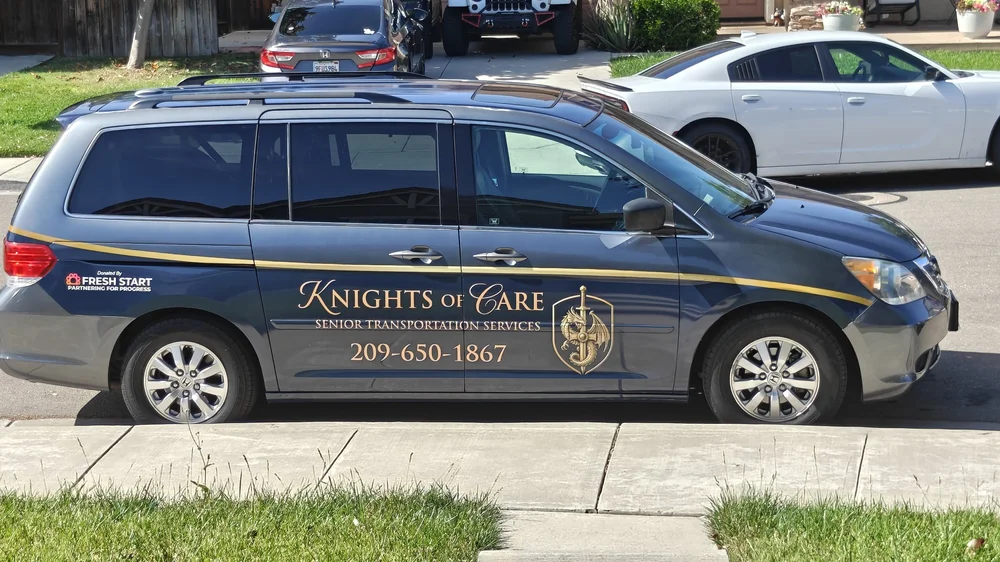 The Knights of Care Honda Odyssey, gray with a navy and gold logo, parked at a residential curb