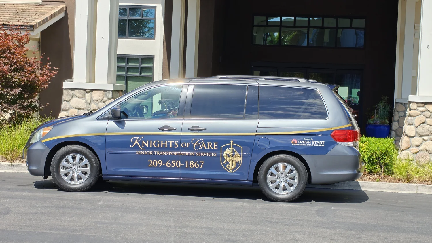 The Knights of Care van, a gray Honda Odyssey with a navy and gold Knights of Care logo and (209) 650-1867 on the side, parked at a building entrance