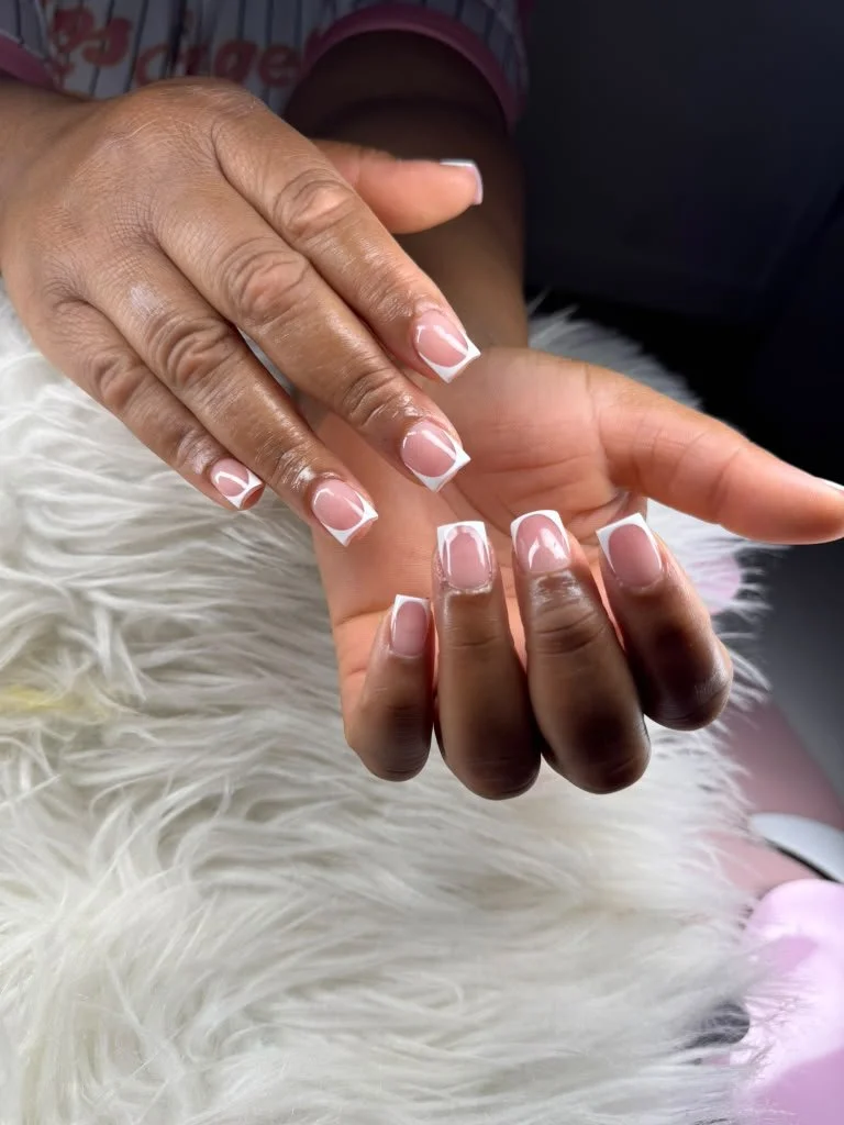 Close-up of two hands displaying fresh French manicure with natural pink nails and white tips, resting on a white furry surface.