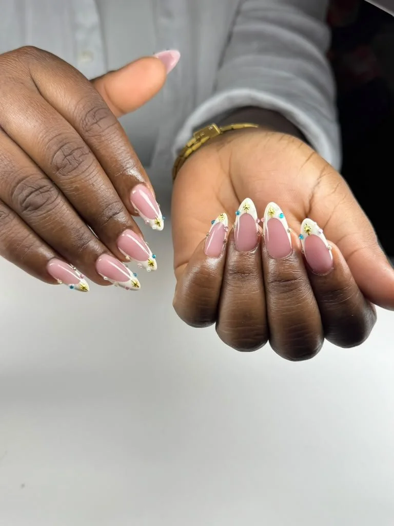 Close-up of hands with decorated nails featuring a white and gold design with small star and dot accents.