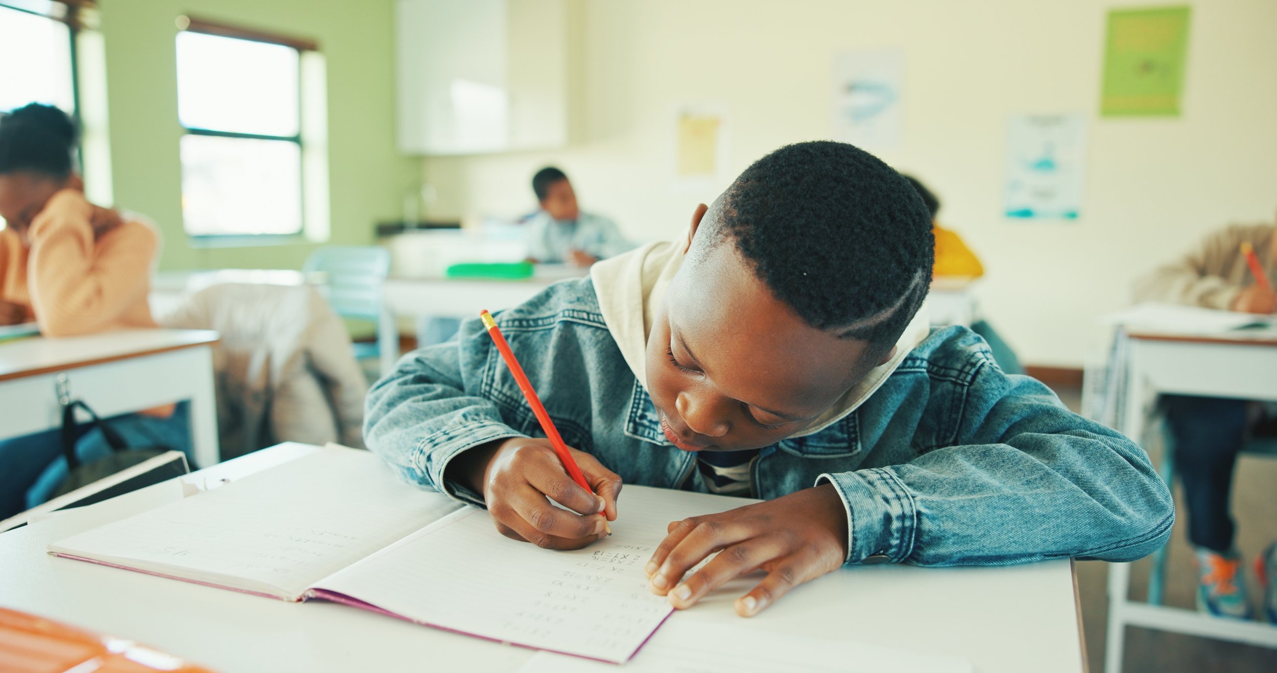 Student writing in a notebook in a classroom.