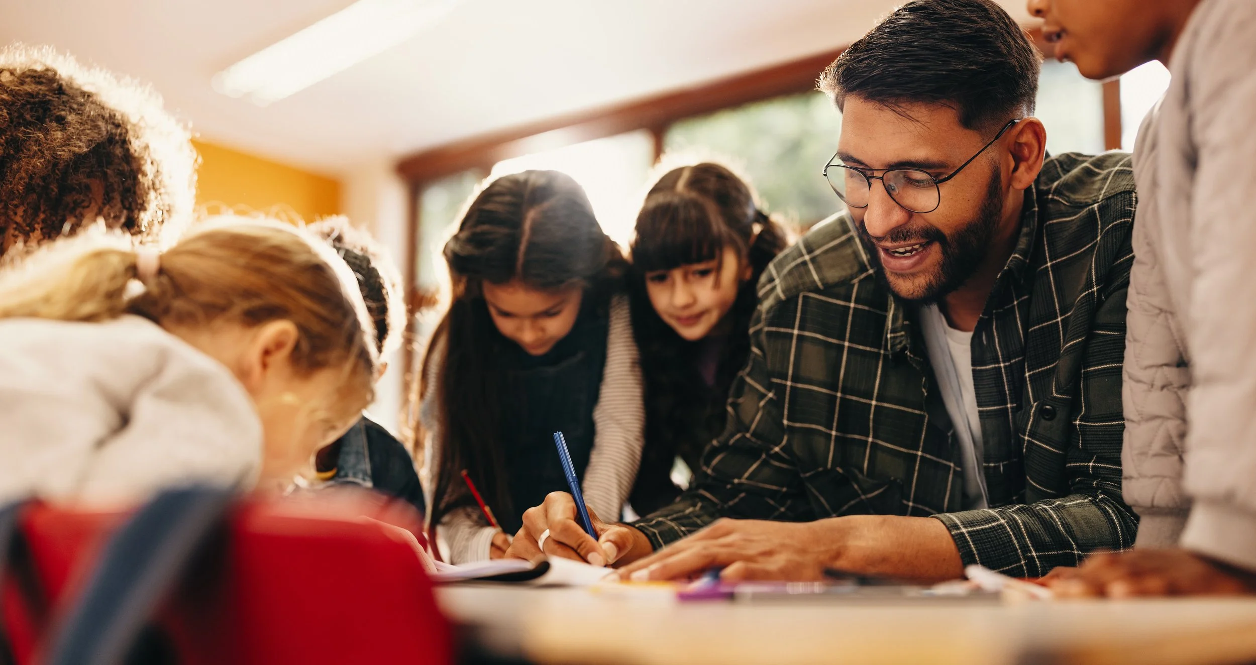 A group of children and an adult male engaging in a study or activity at a table indoors.