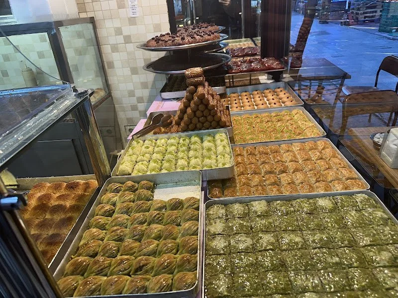 Assorted Middle Eastern pastries and desserts displayed in metal trays on a bakery or café counter.
