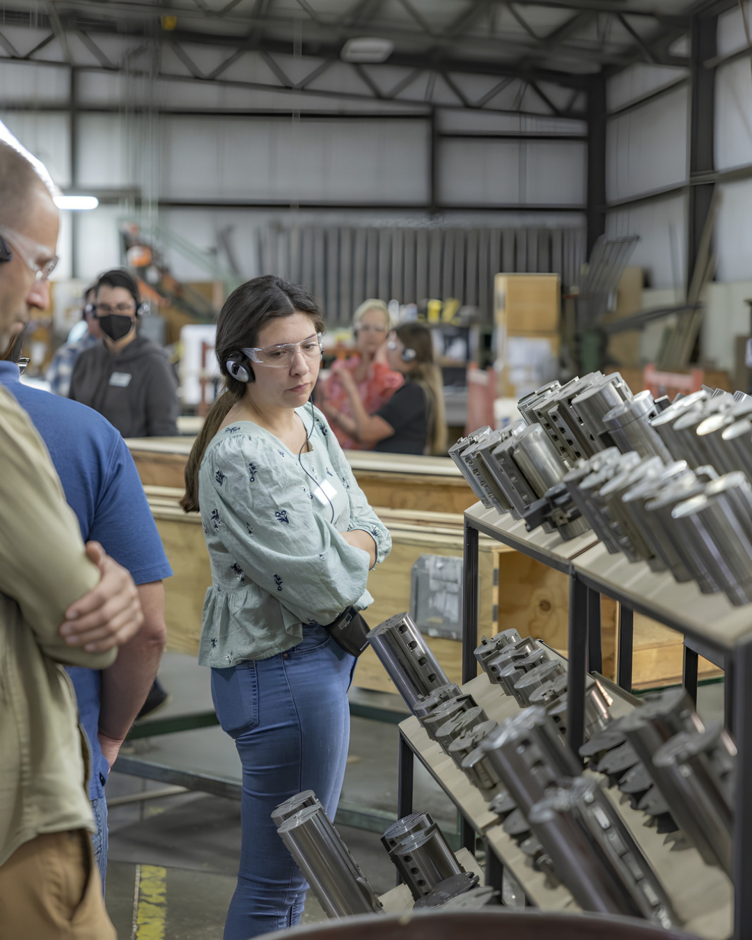 Anna Thompson examining equipment during a workshop visit, wearing hearing protection and safety glasses.