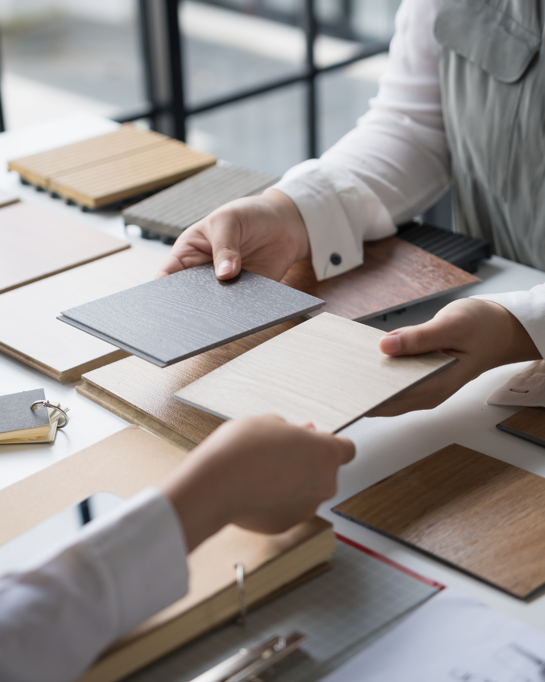 Two people comparing wood and surface finish samples on a table.