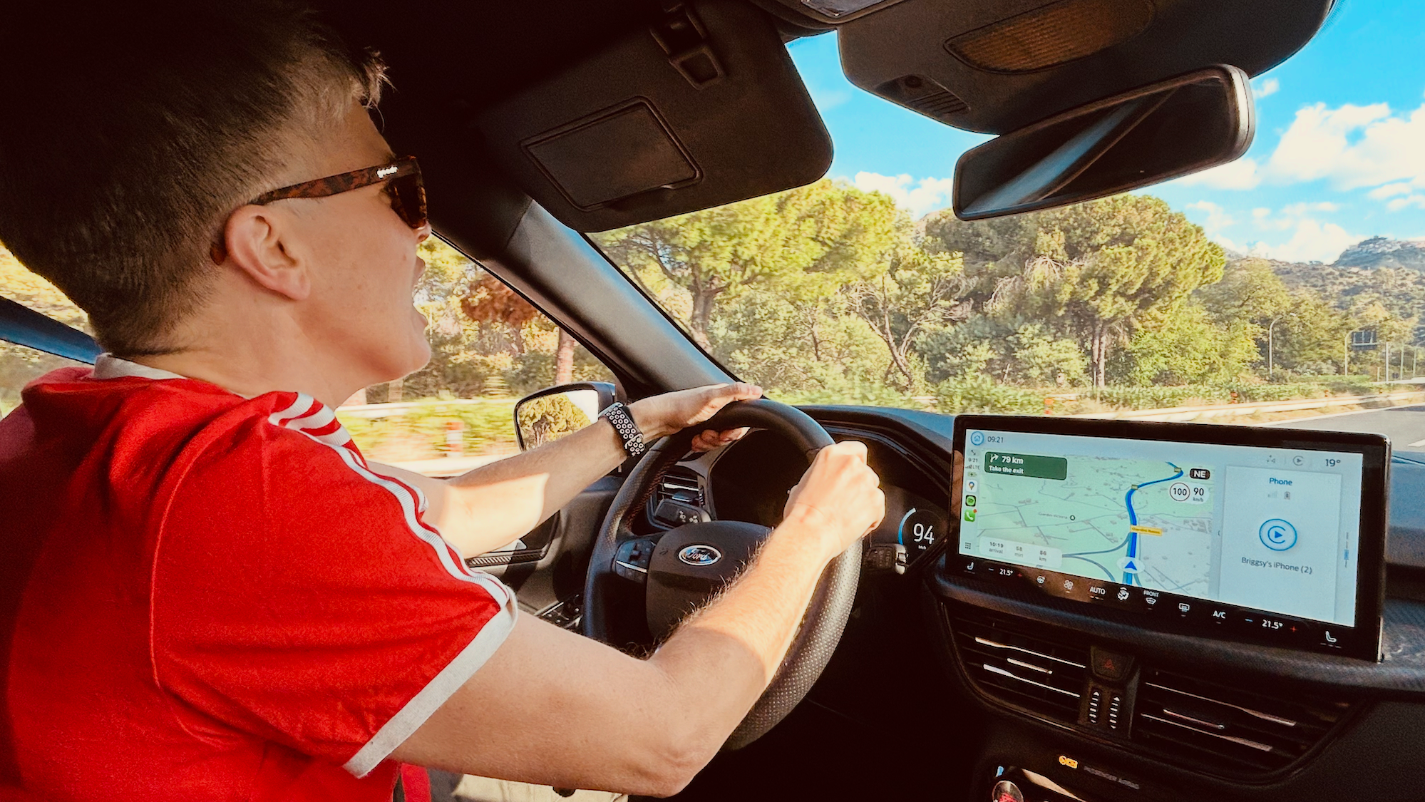 Traveler driving a rental car on a sunny road in Sicily, with navigation displayed on the dashboard.
