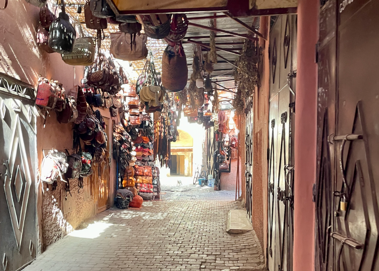 Narrow covered lane in the Marrakech medina lined with shops and hanging goods.