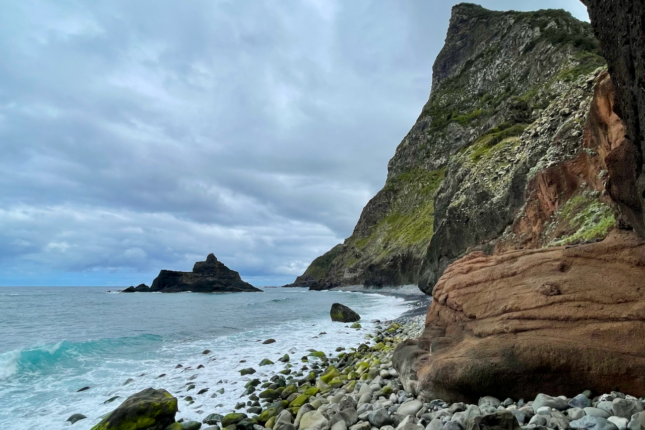 Rocky coastline and turquoise Atlantic water beneath steep green cliffs in Madeira.