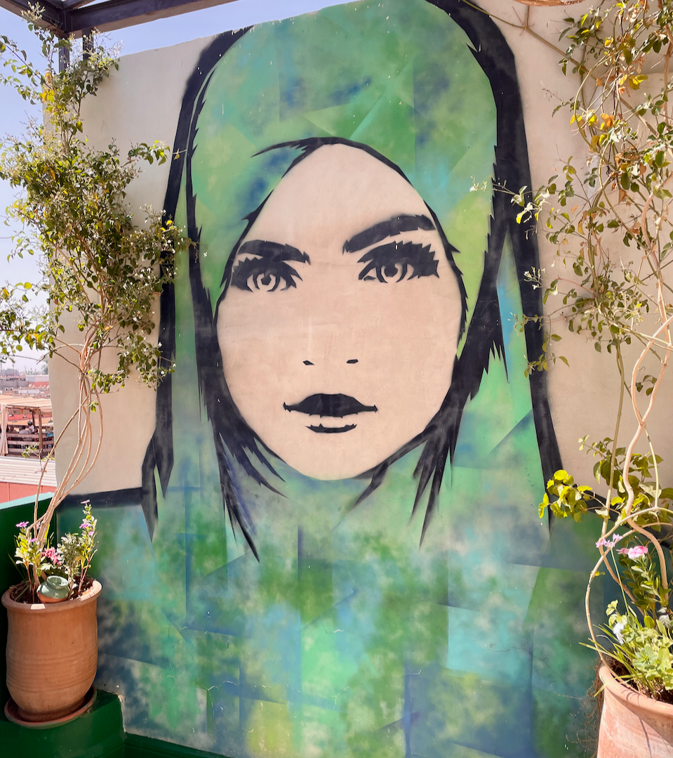 Large green-and-blue mural of a woman in a headscarf at a rooftop restaurant in Marrakech.