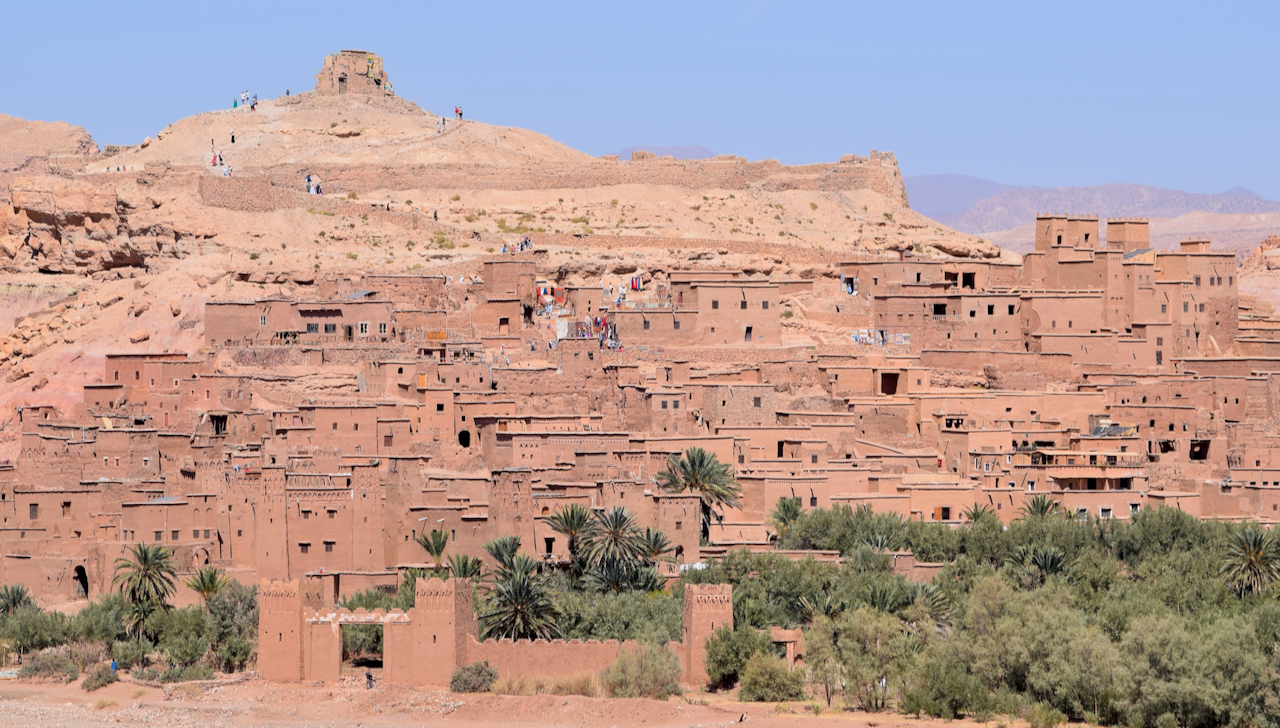 Earthen buildings of the fortified ksar of Aït-Ben-Haddou rising above a palm-lined valley in Morocco.