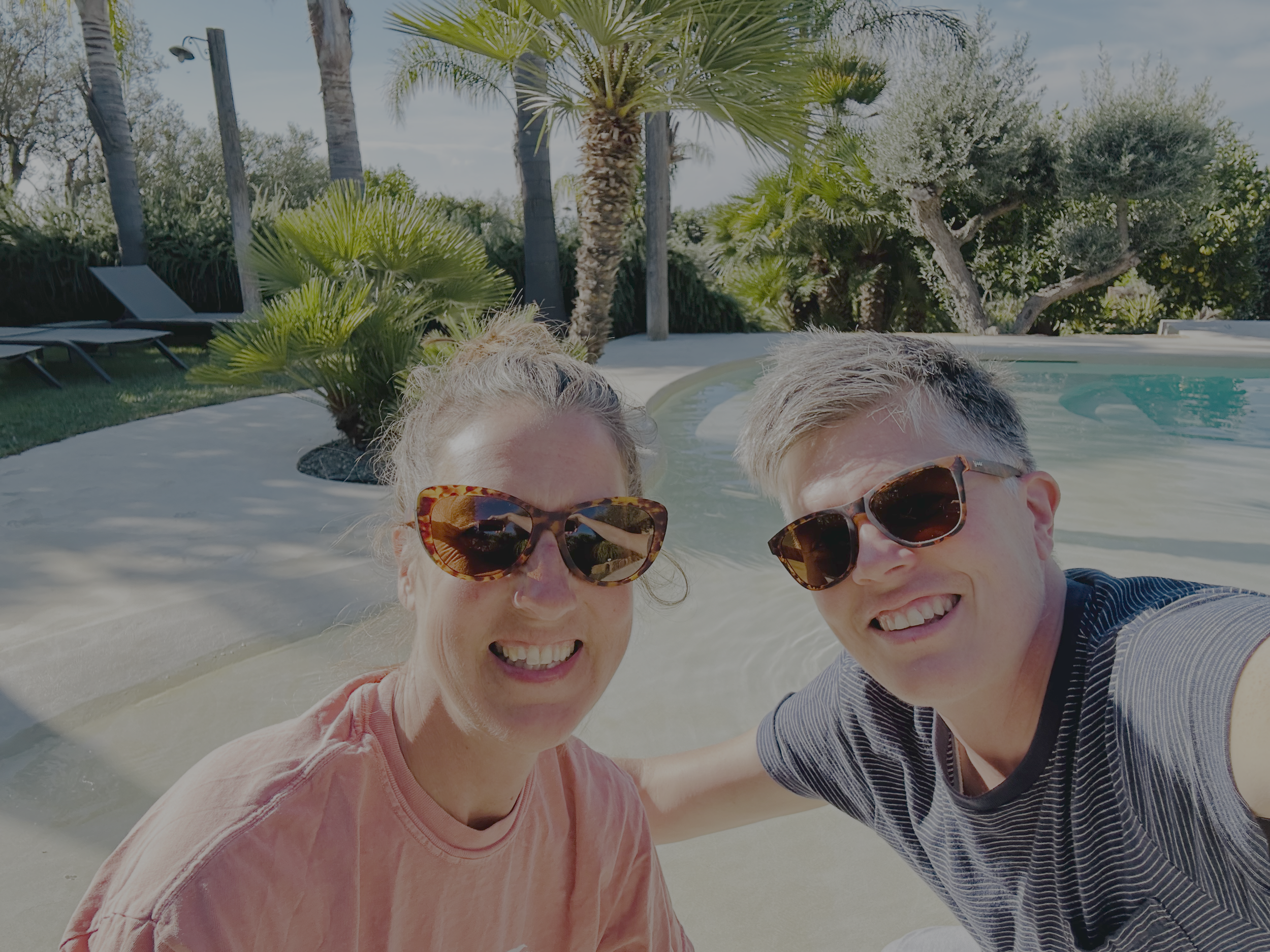 Briggs and Sonja smiling beside a hotel pool in Sicily.