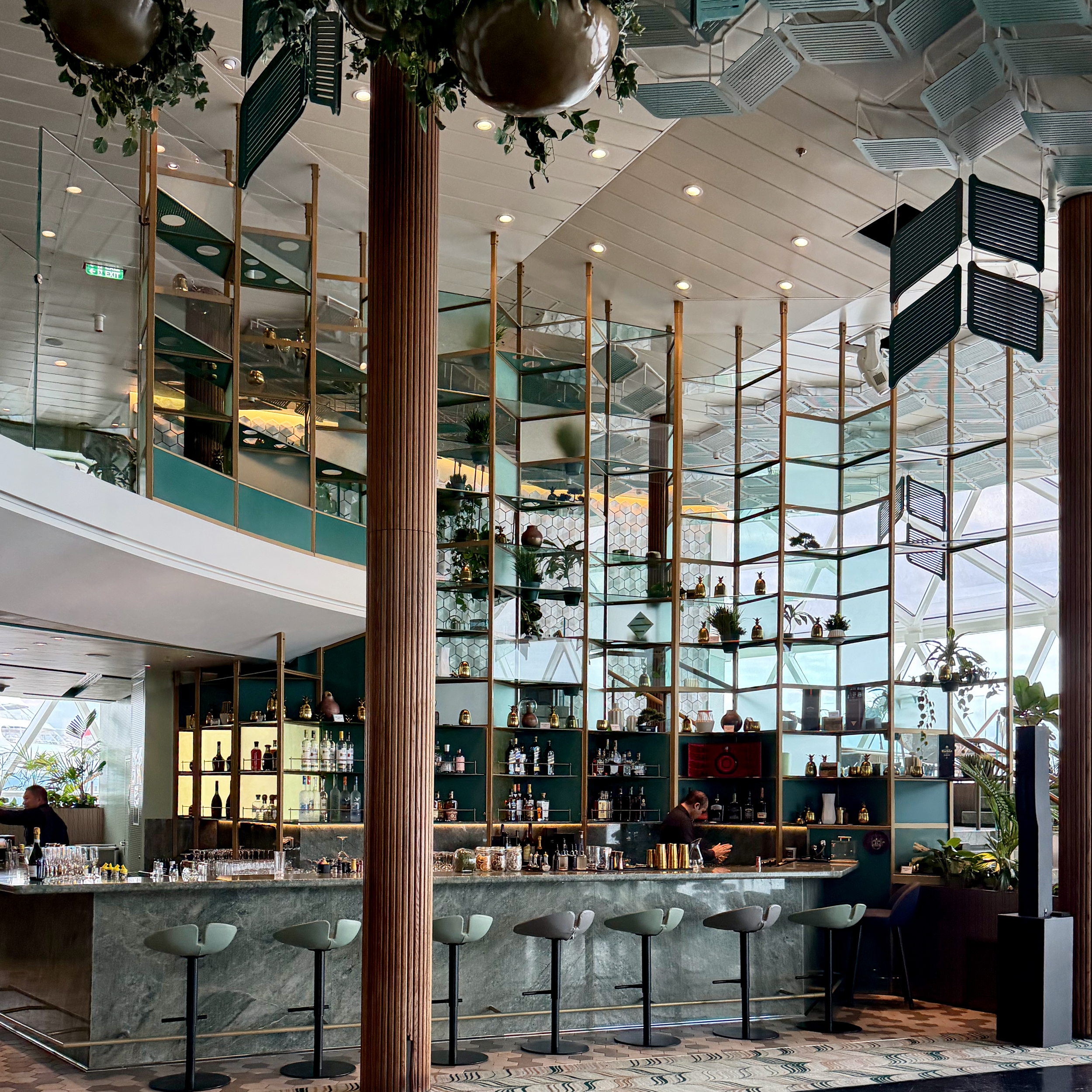 1. A bright, contemporary bar aboard Celebrity Edge with floor-to-ceiling windows and greenery.