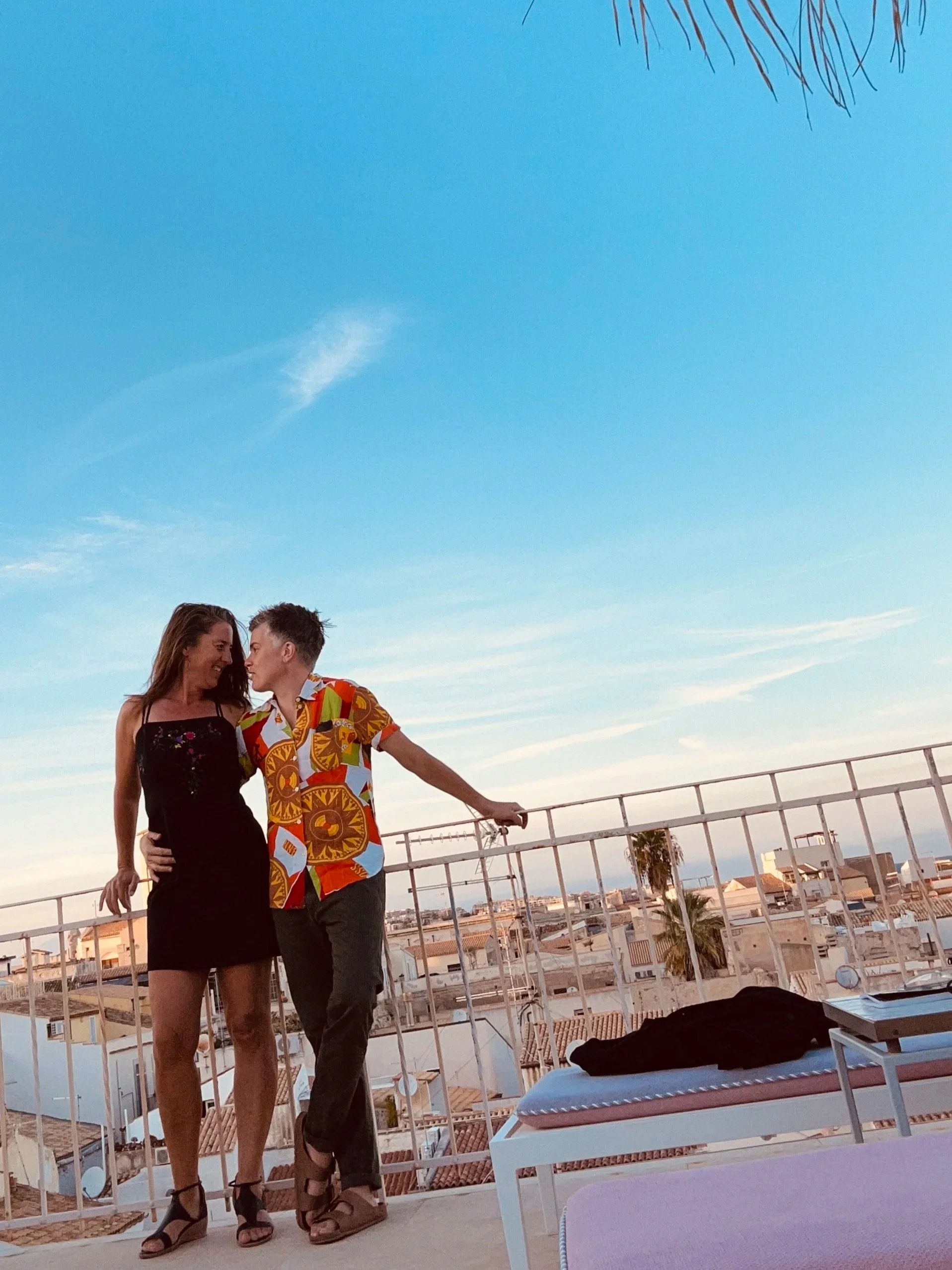 1. Two travelers standing together on a terrace overlooking a coastal town in Sicily.