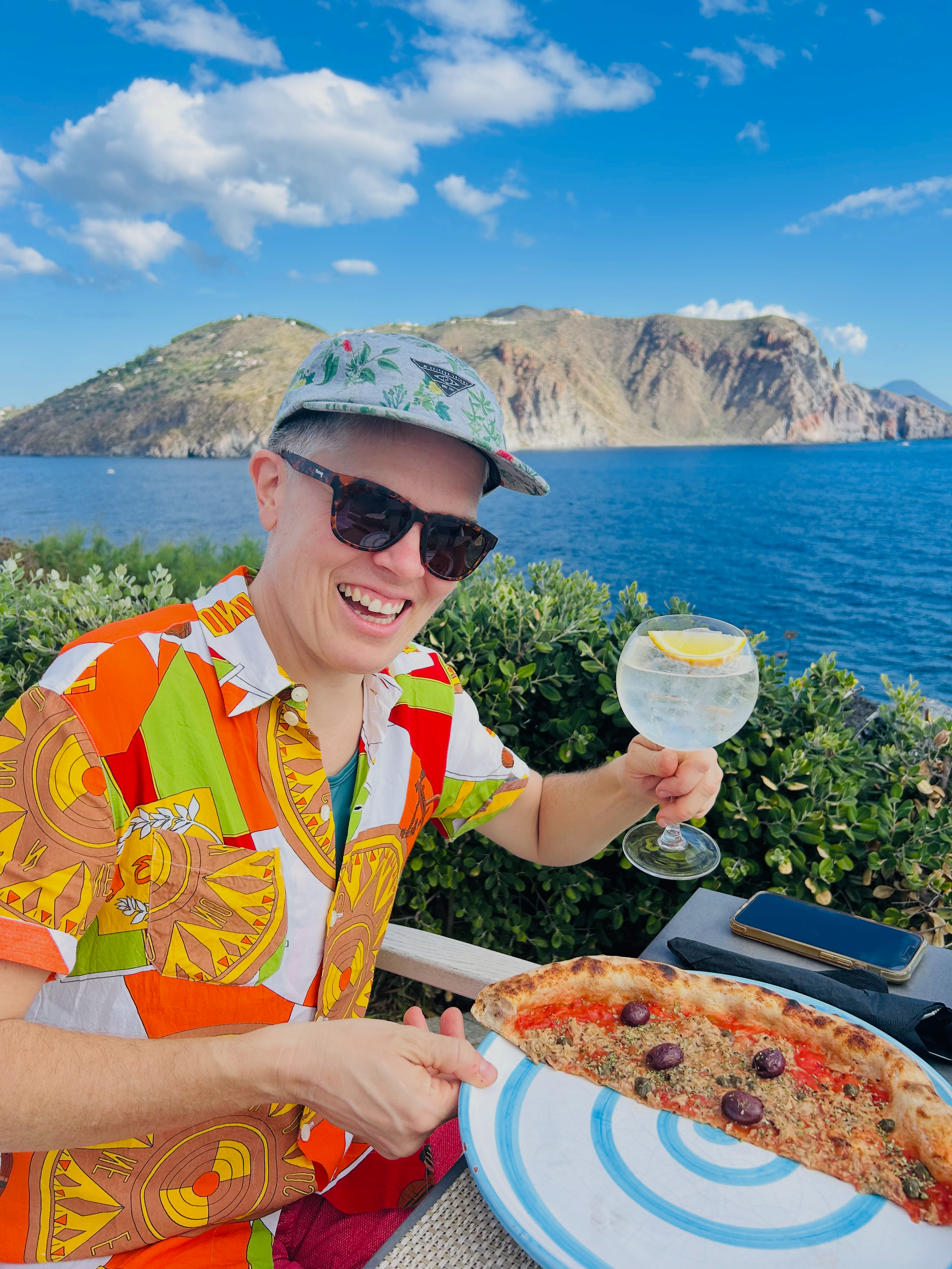 1. Traveler holding a pizza and drink on a terrace overlooking the sea in Sicily.