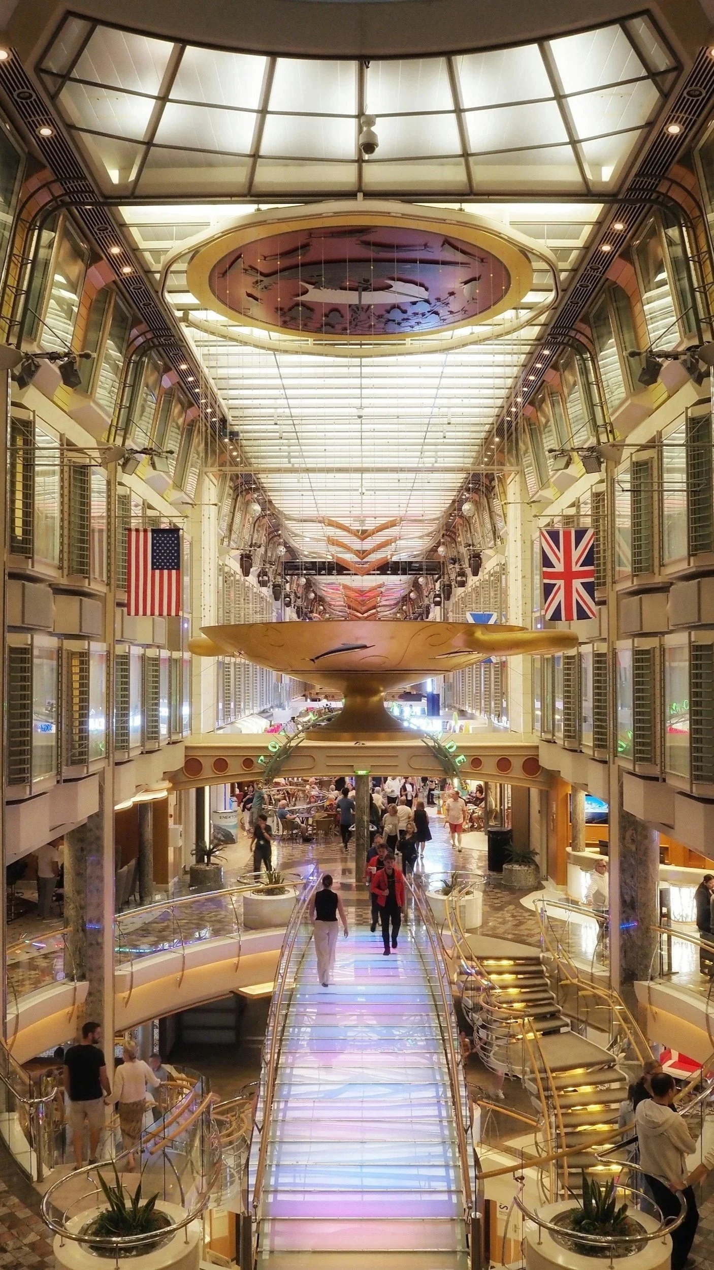 A multi-level cruise ship interior with shops, dining, and a brightly lit central promenade.