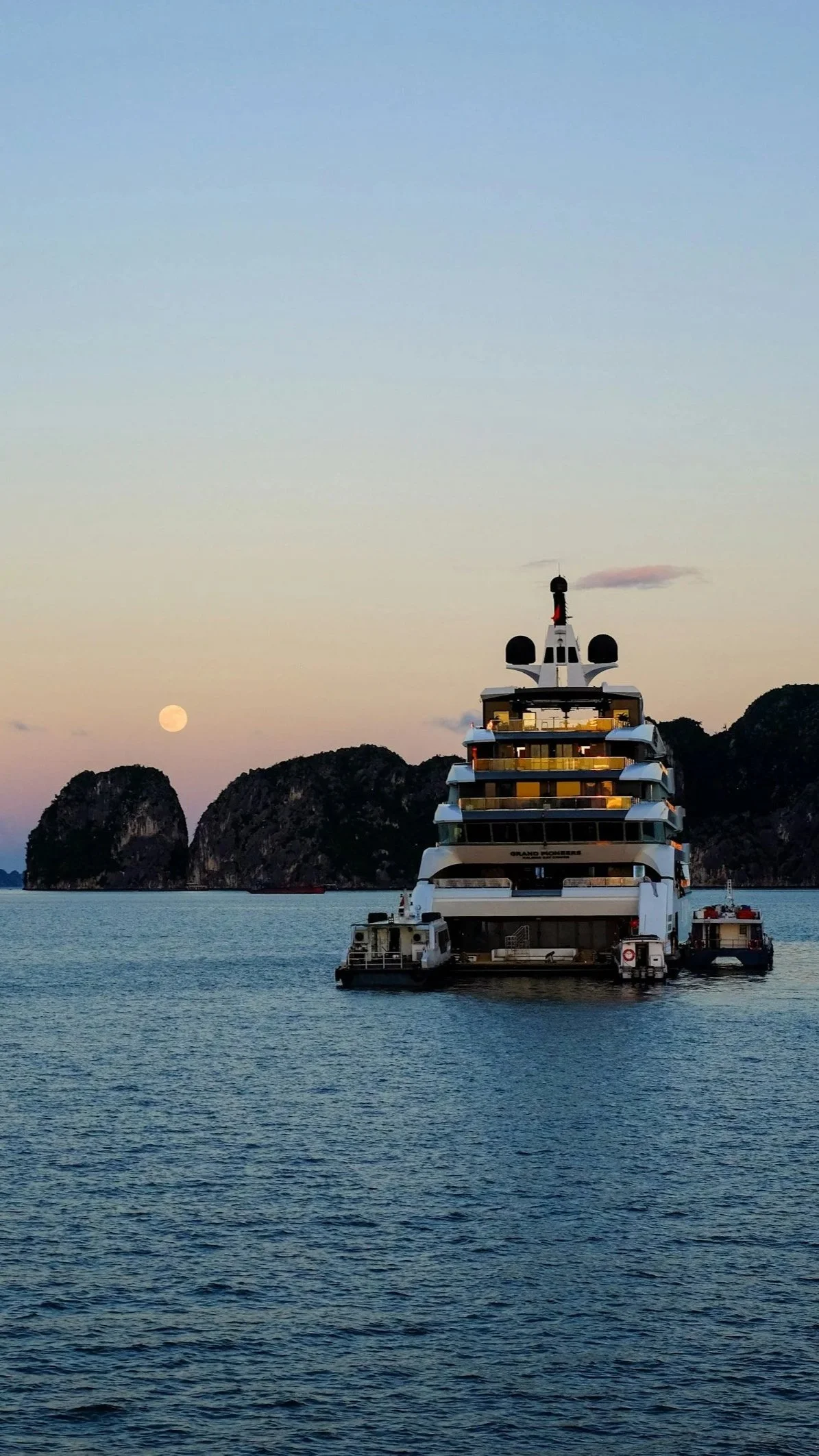 A small luxury ship anchored near rocky islands at sunset.