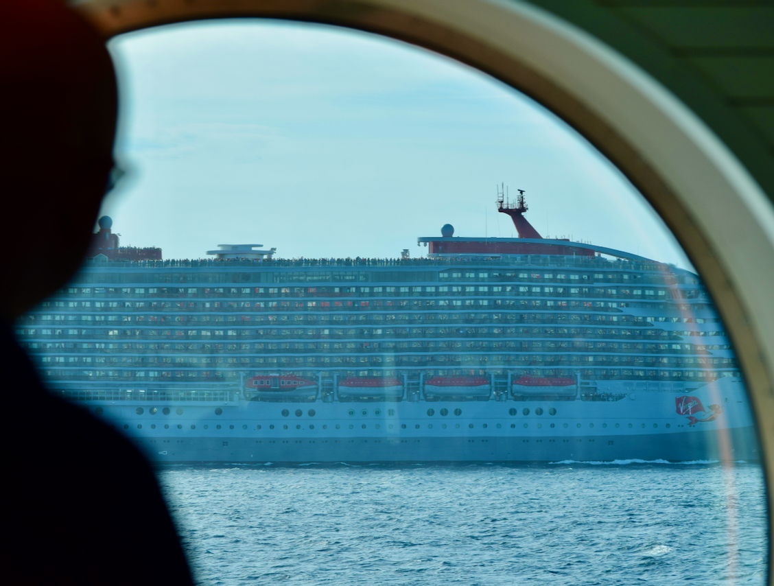 A large cruise ship seen through a round ship window while underway.
