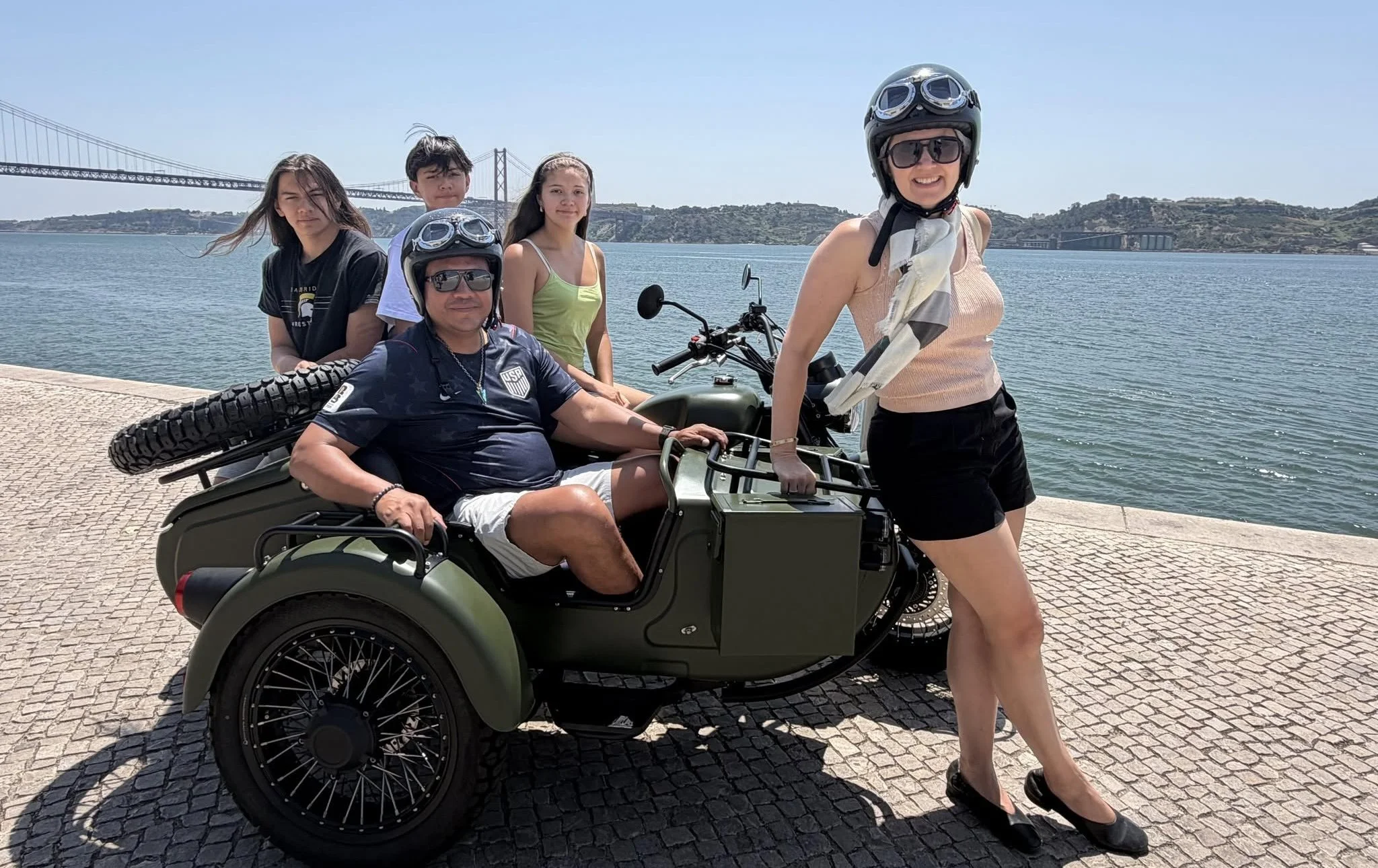 A small group posing around a motorcycle and sidecar on Lisbon’s waterfront.