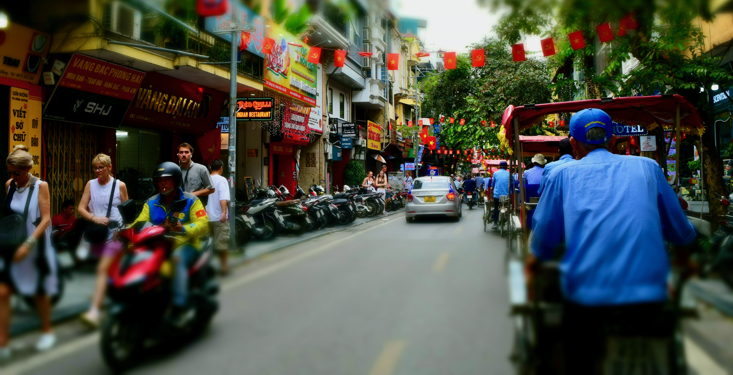 1. A busy Southeast Asian city street with motorbikes, pedestrians, shops, and traffic.