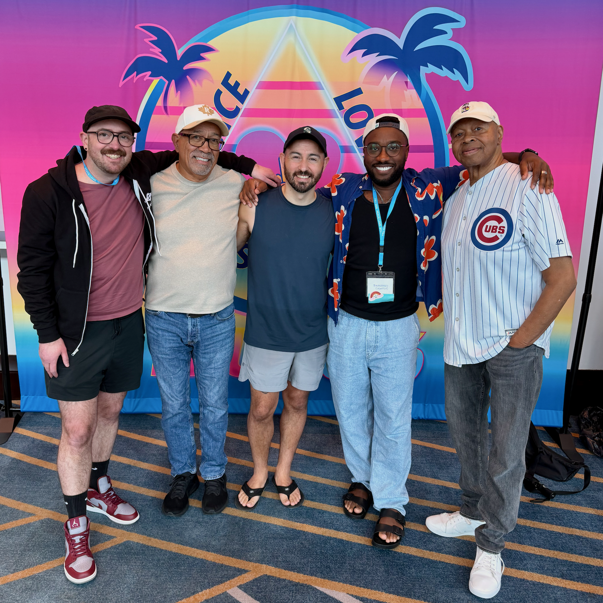 A group of 5 friends smile as they pose in front of a banner at a recovery conference.