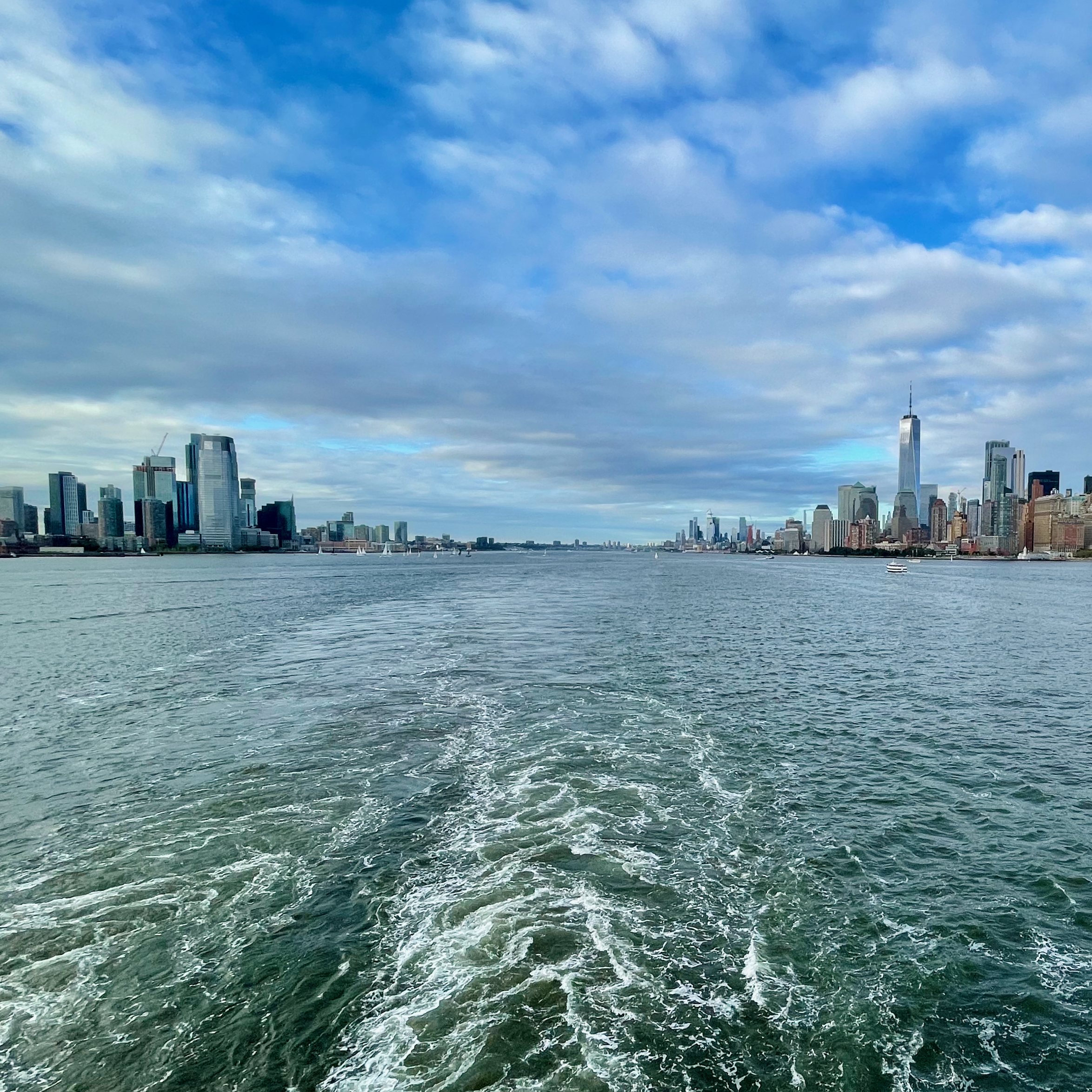 Cruise ship wake crossing New York Harbor with the Manhattan skyline in the distance.
