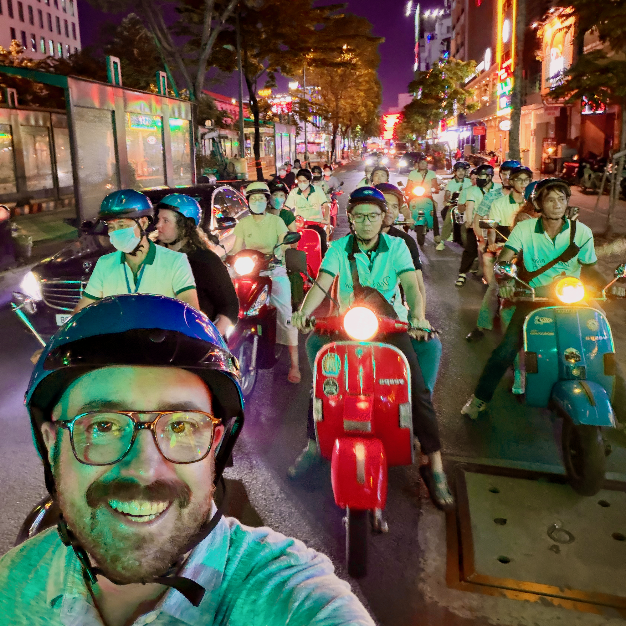 A traveler riding through a busy city at night with motorbikes and illuminated storefronts behind him.