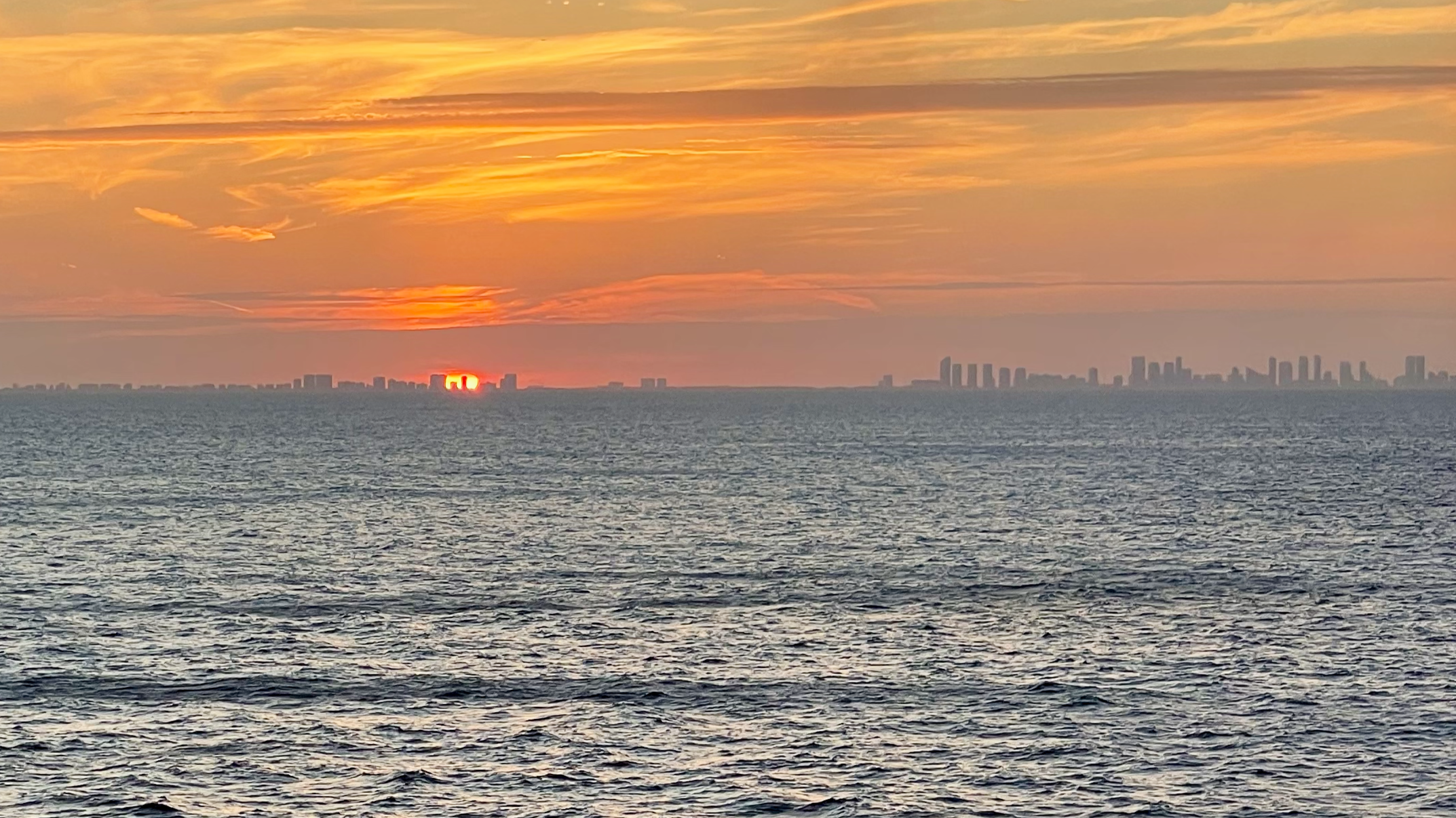 Sunset over the ocean as the ship leaves Miami, with the city skyline on the horizon.