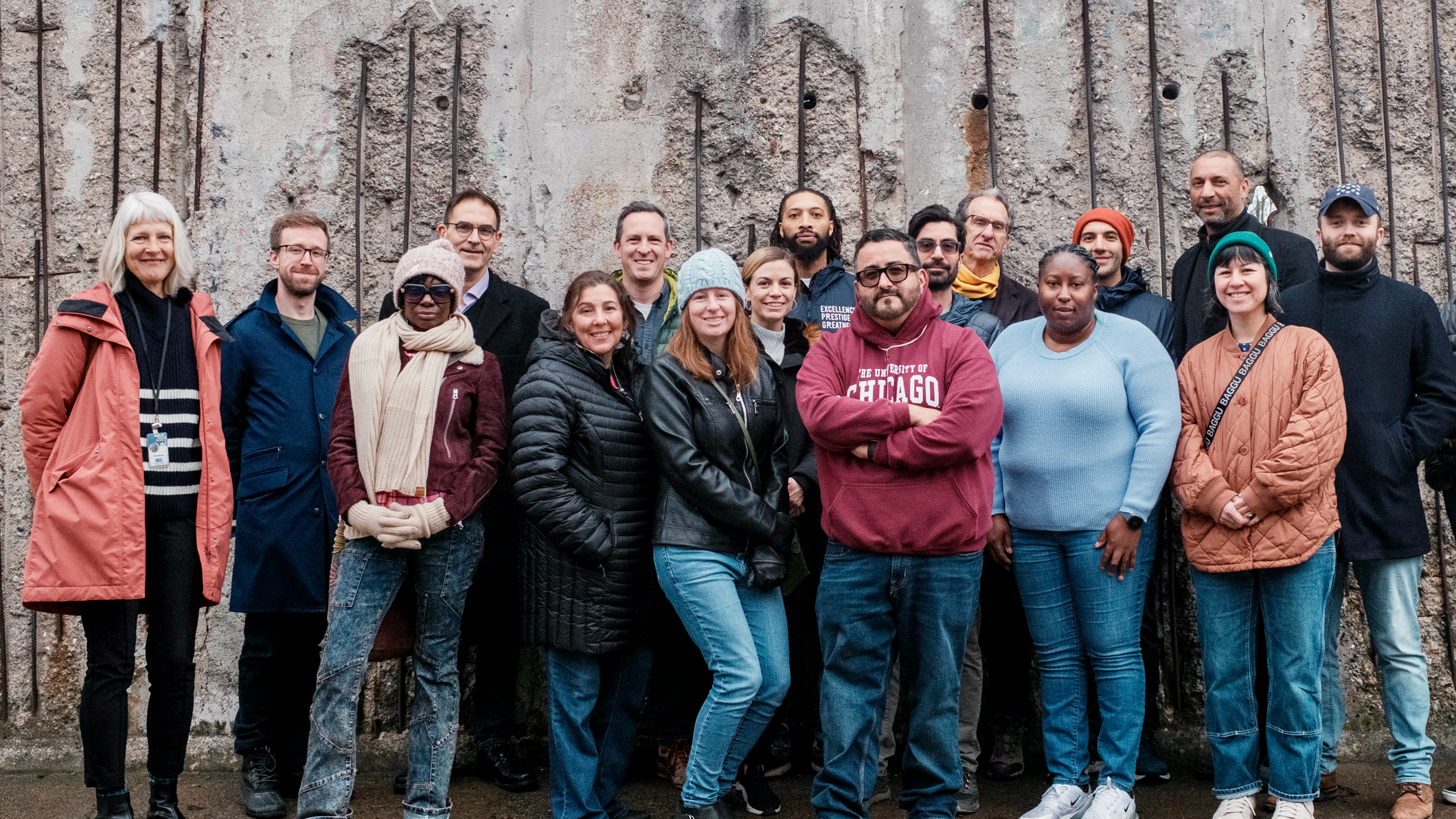 A group of adult travelers standing together outdoors in front of a section of the Berlin Wall.