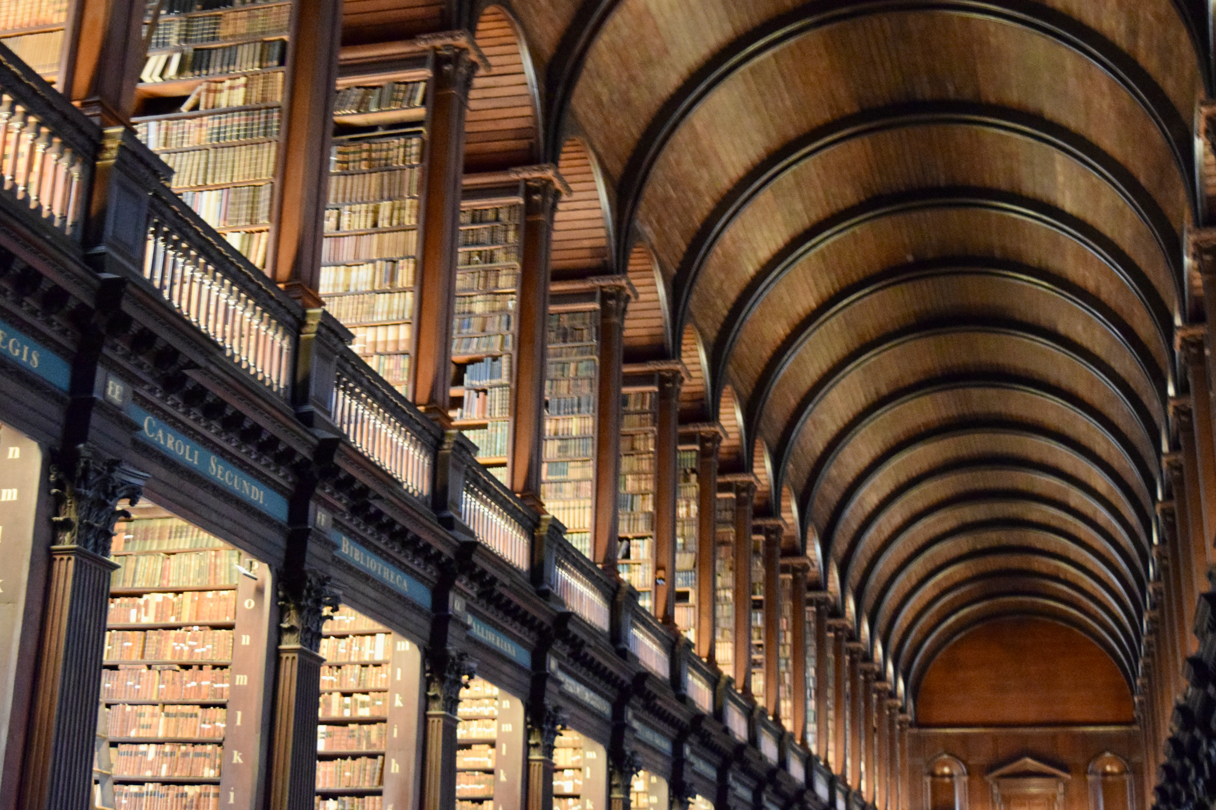 A grand historic library with floor-to-ceiling bookshelves beneath a long arched wooden ceiling.