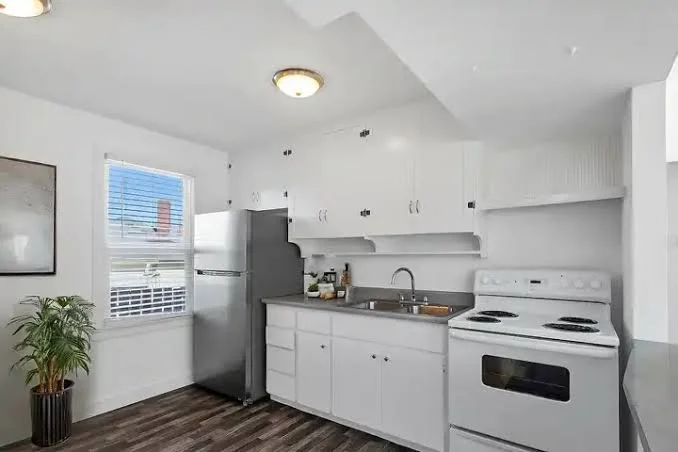 Kitchen with white cabinets, a stainless steel refrigerator, white stove, and a window with blinds.
