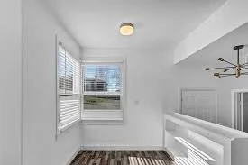 Empty room with white walls, two windows with blinds, a ceiling light, and hardwood flooring.