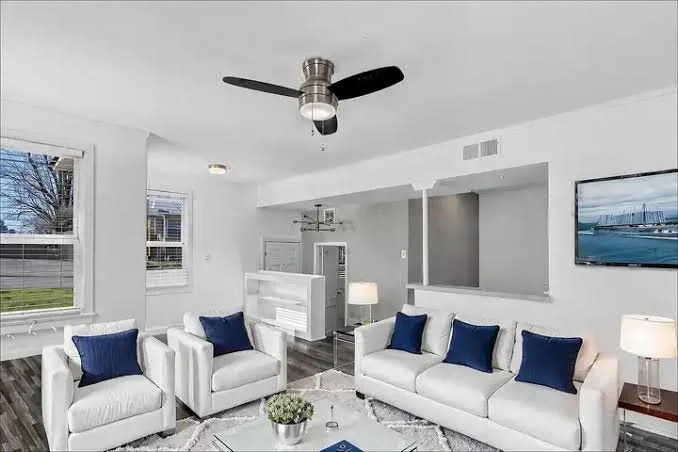Living room with white furniture, blue pillows, a ceiling fan, and a mounted TV.