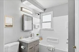 Bathroom with a white vanity, mirror, toilet, window, and shower area